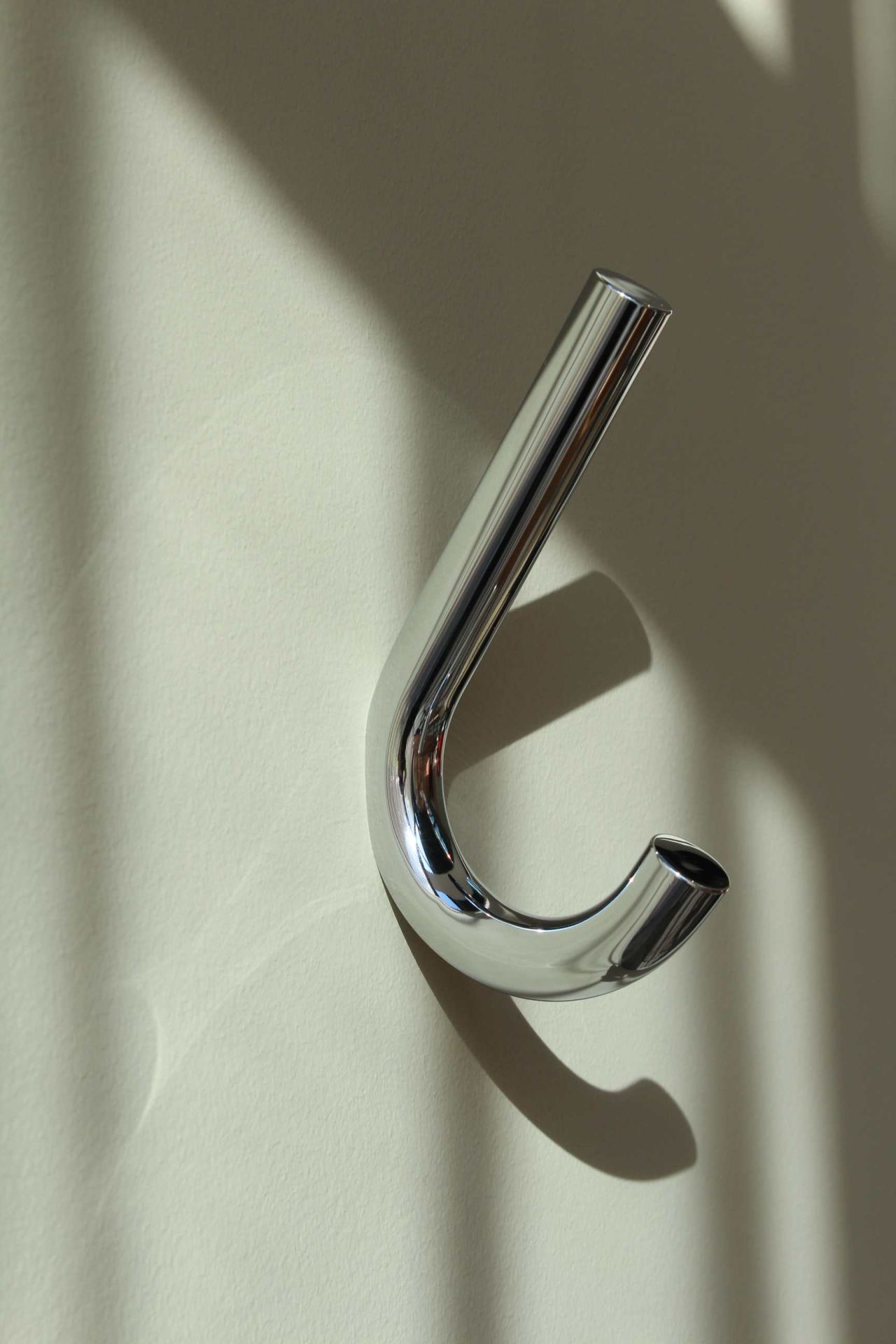 Nahaufnahme des verchromten Thonet S 12 Wandhakens an einer hellen Wand mit Schatten.