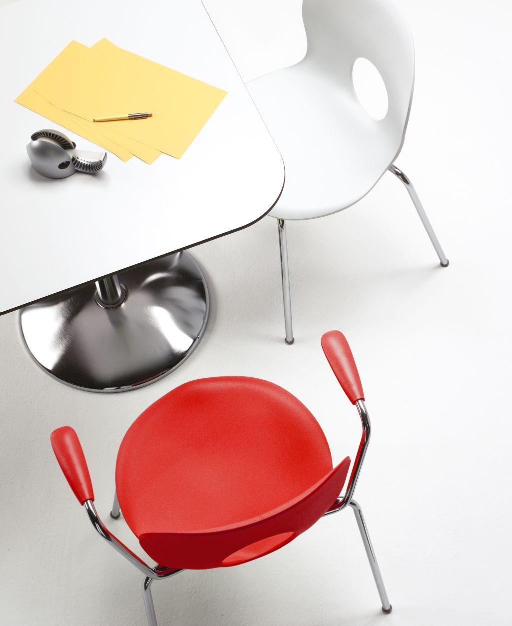 Zanziplano Tisch von Rexite mit rotem und weißem Stuhl, gelben Blättern und silbernem Briefbeschwerer.