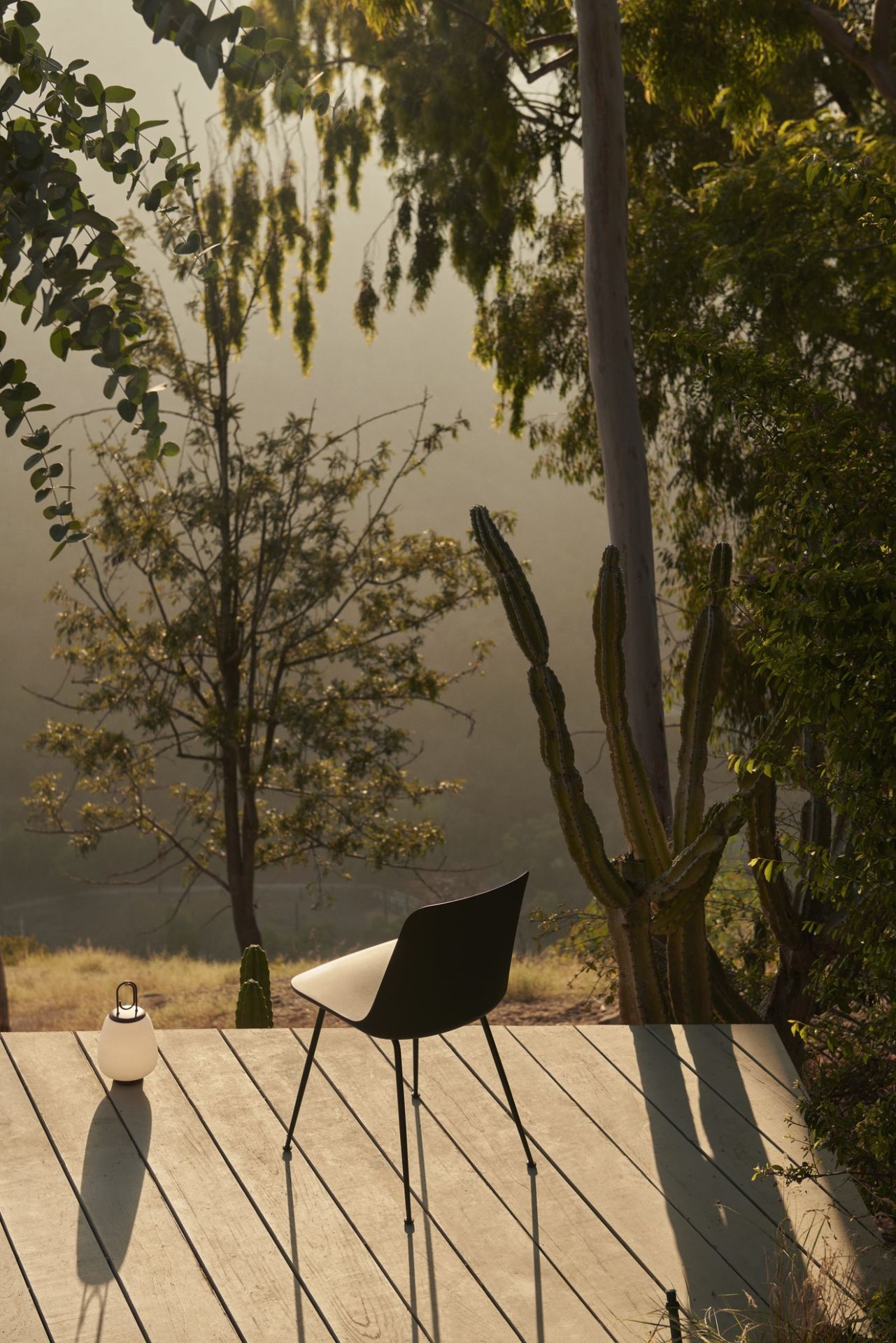 Schwarzer AndTradition Rely HW70 Outdoor Stuhl auf Holzterrasse mit Lampe und Garten im Hintergrund.