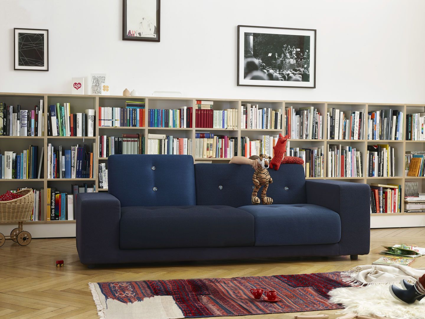 Blaues Polder Sofa von Vitra vor Bücherregal, mit Spielzeug dekoriert, auf Parkettboden mit Teppich.