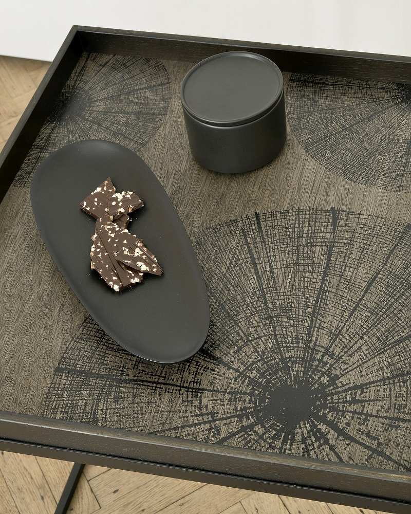 Detailaufnahme: Ethnicraft Tray Tablett für quadratischen Couchtisch mit Schokolade und Dose auf Holzoberfläche mit Baumringmuster.