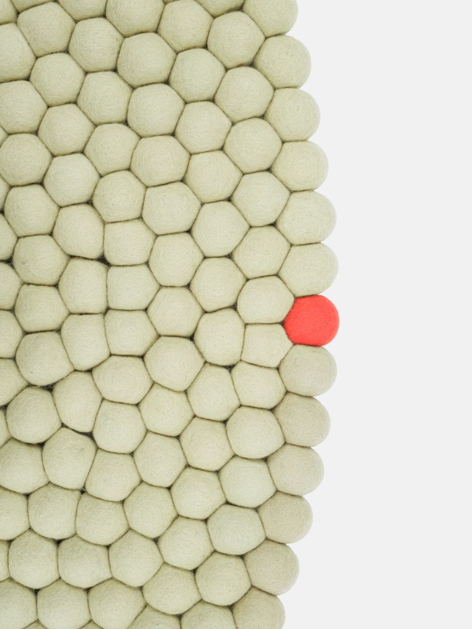 Detailaufnahme: Grünbeiger Filzteppich "Big One" aus runden Filzkugeln, mit einer roten Kugel.
