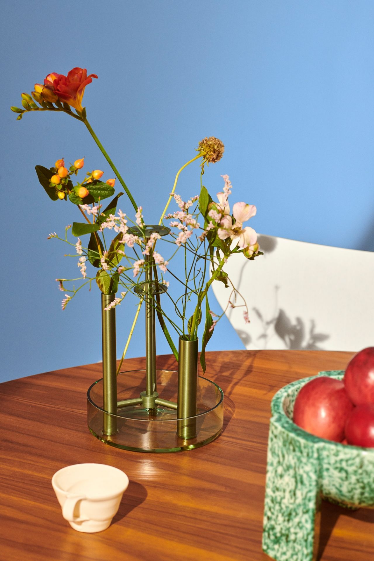Ikeru Vase von Fritz Hansen mit Blumen auf einem Holztisch vor blauem Hintergrund.