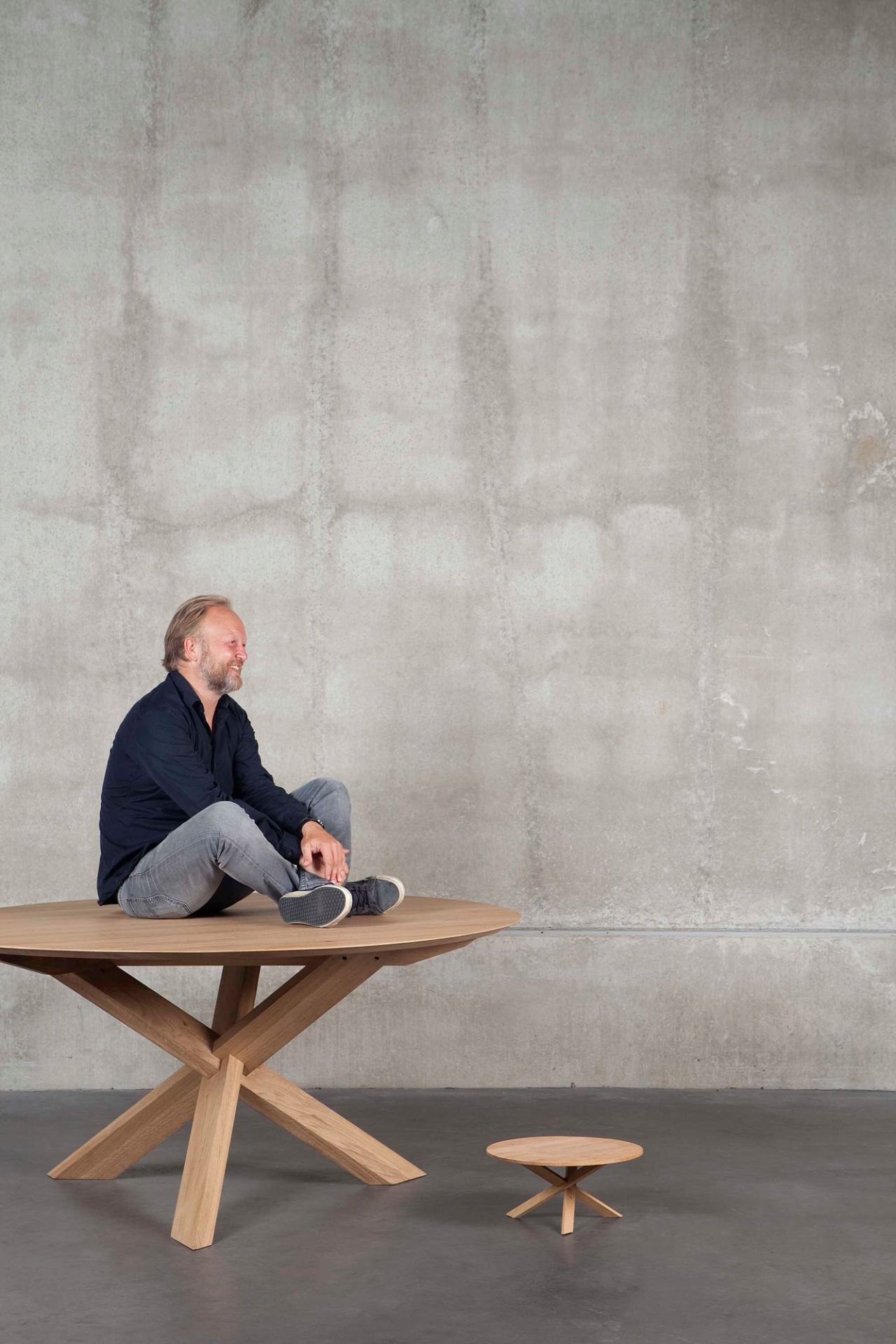 Esstisch Circle von Ethnicraft aus Eiche mit Mann darauf, runder Holztisch mit Kreuzgestell.