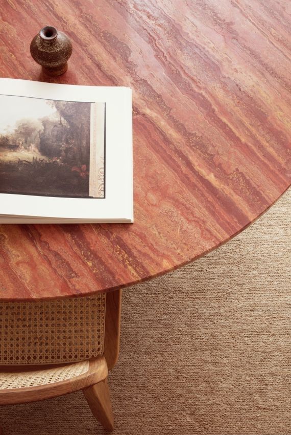 Detailaufnahme des Epic Esstischs von Gubi mit roter Travertin-Tischplatte, Buch und Vase.