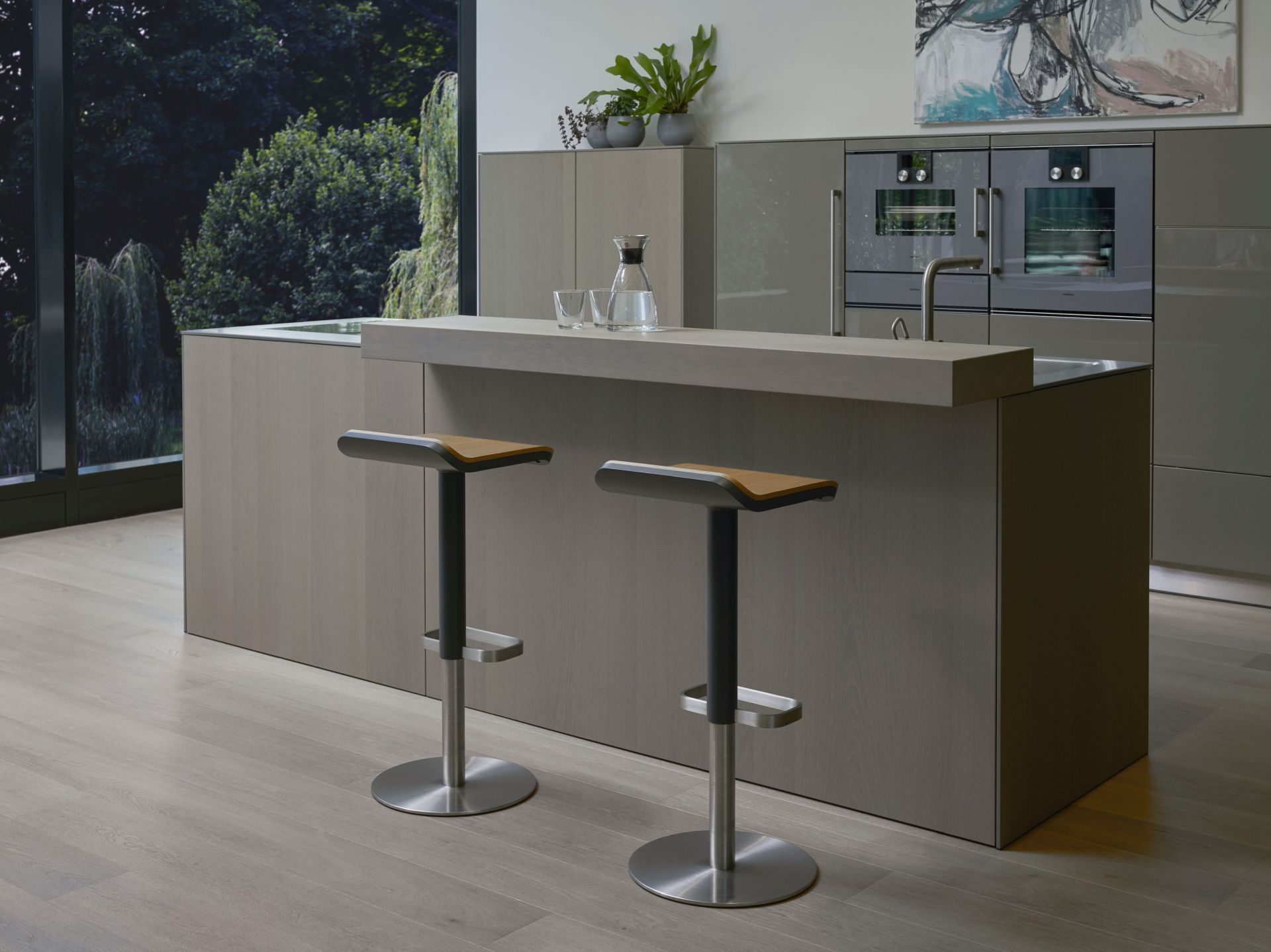 Zwei ED Barhocker mit Edelstahlgestell und Eiche-Sitz vor moderner Kücheninsel. Höhenverstellbare Barstühle für Esszimmer und Küche.