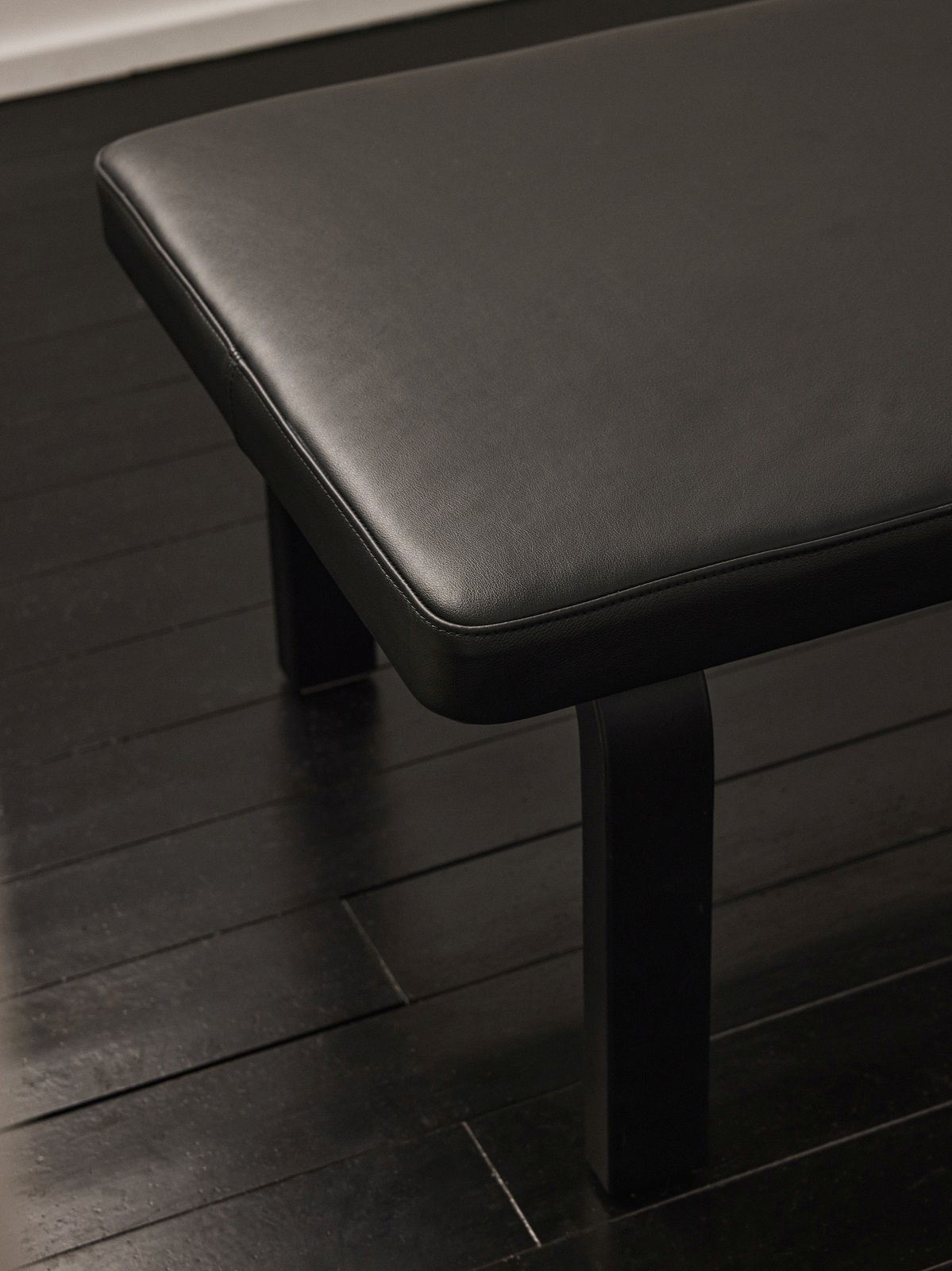 Detailaufnahme der schwarzen Artek Bank 167 mit Lederbezug und dunklem Holzfuß auf dunklem Holzboden.