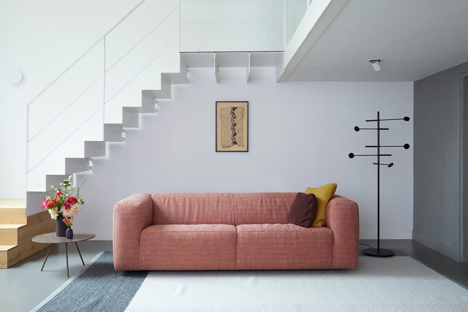 Wohnzimmer mit Kingpin Floor Stehleuchte Japth, Sofa, Teppich und Treppe in modernem Design.