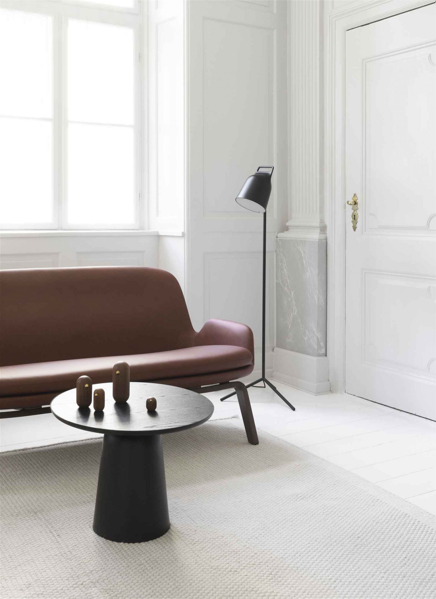 Schwarzer Normann Copenhagen Turn Table Tisch mit Holzfiguren in modernem Wohnzimmer mit Sofa und Stehlampe.