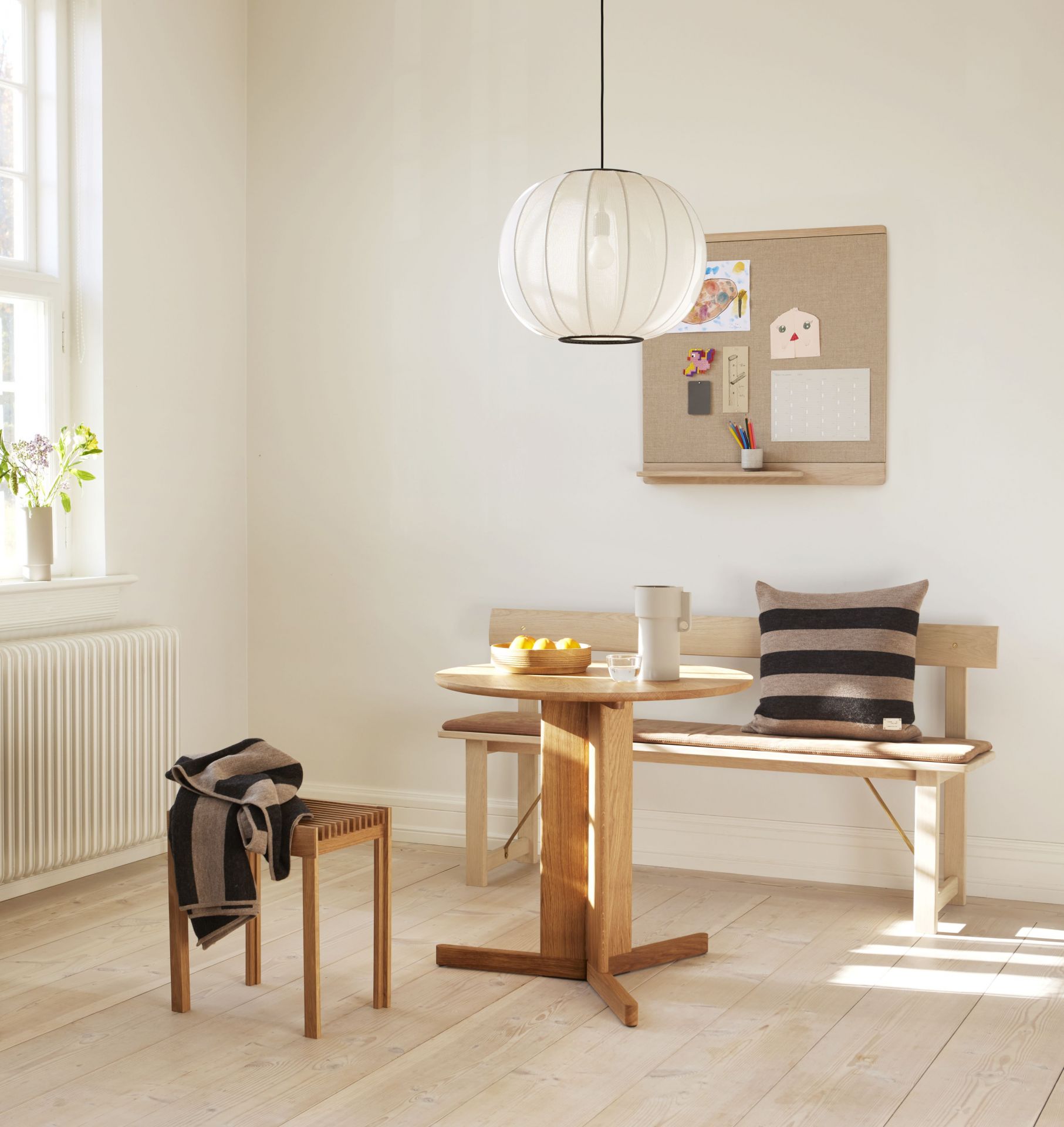 Helles Esszimmer mit Rim Pinnwand, Holztisch, Bank und Stuhl. Dekorative Wohnaccessoires und Lampe.