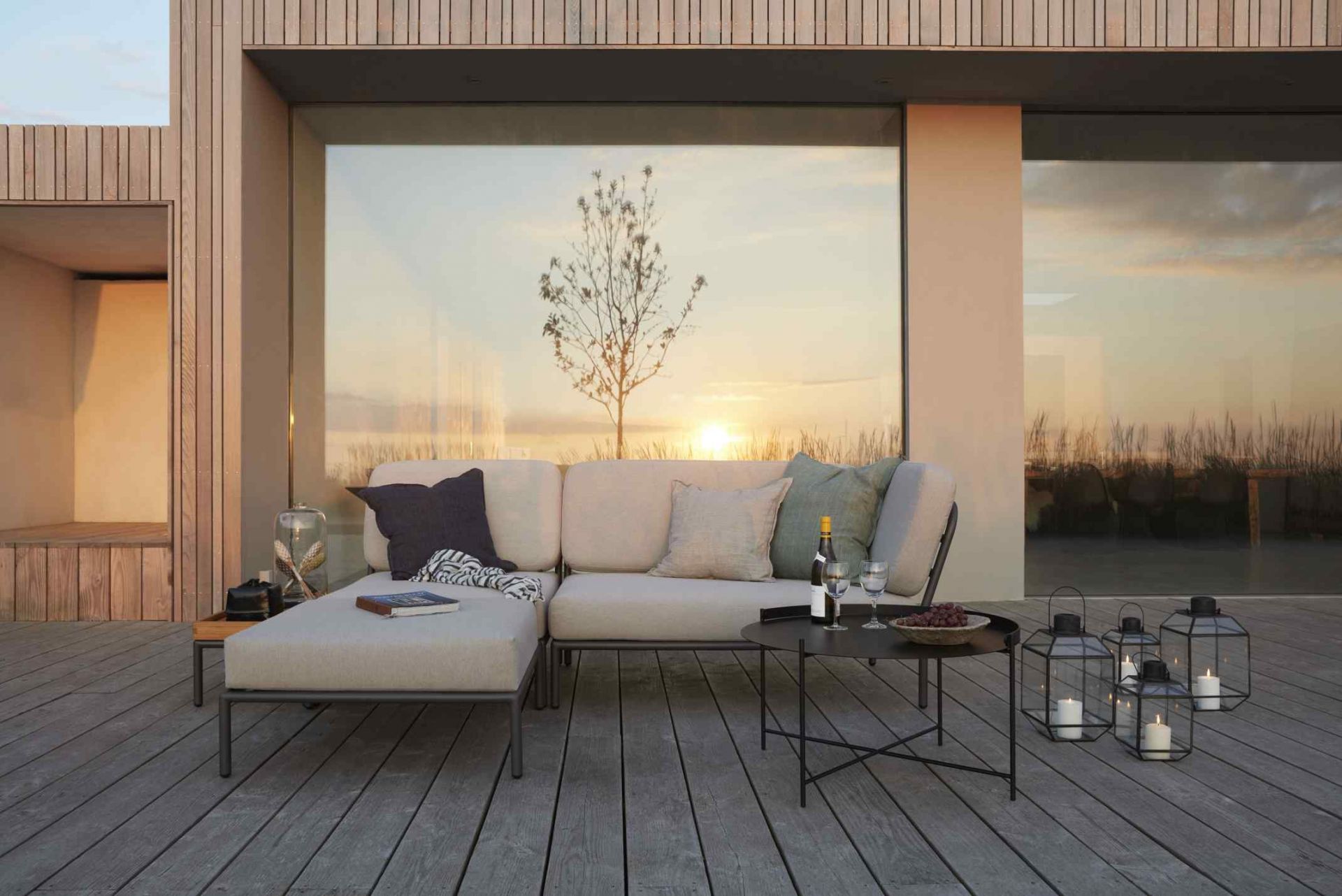 Houe Level Beistelltisch Outdoor neben Lounge-Möbeln auf Holzterrasse mit Laternen und Abendsonne.