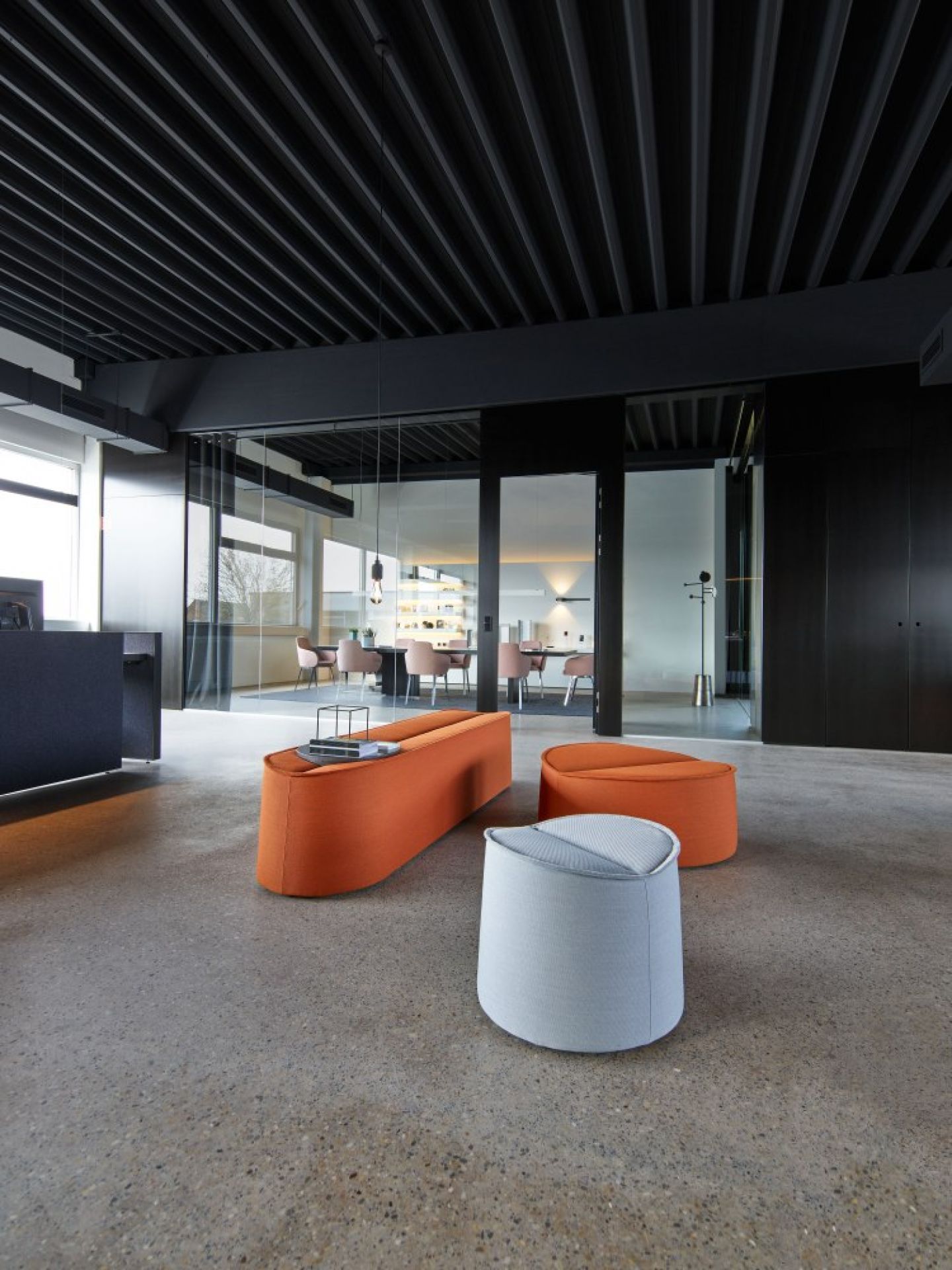 Moderner Büroraum mit orangefarbenen und grauen Sitzmöbeln, darunter ein Bank Cor ähnliches Design.