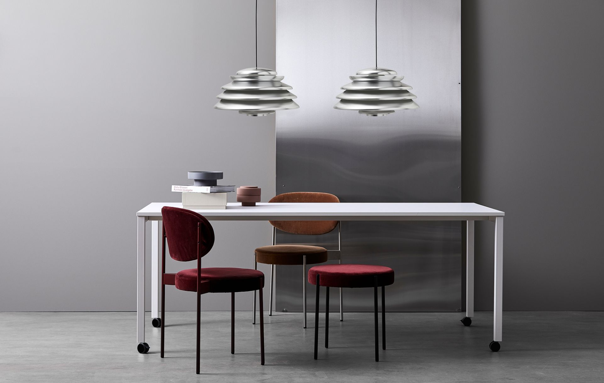 Zwei Verpan Hive Pendelleuchten aus Aluminium hängen über einem weißen Tisch mit Stühlen.