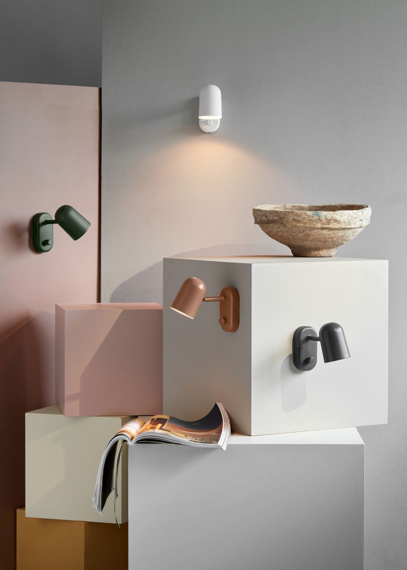 Mehrere Buddy Wandleuchten von Northern in verschiedenen Farben auf gestapelten Blöcken.