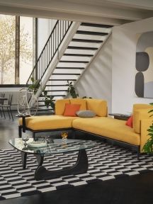 Gelbes Sofa mit Vitra Kissen in Orange und Gelb in modernem Wohnzimmer mit Treppe.