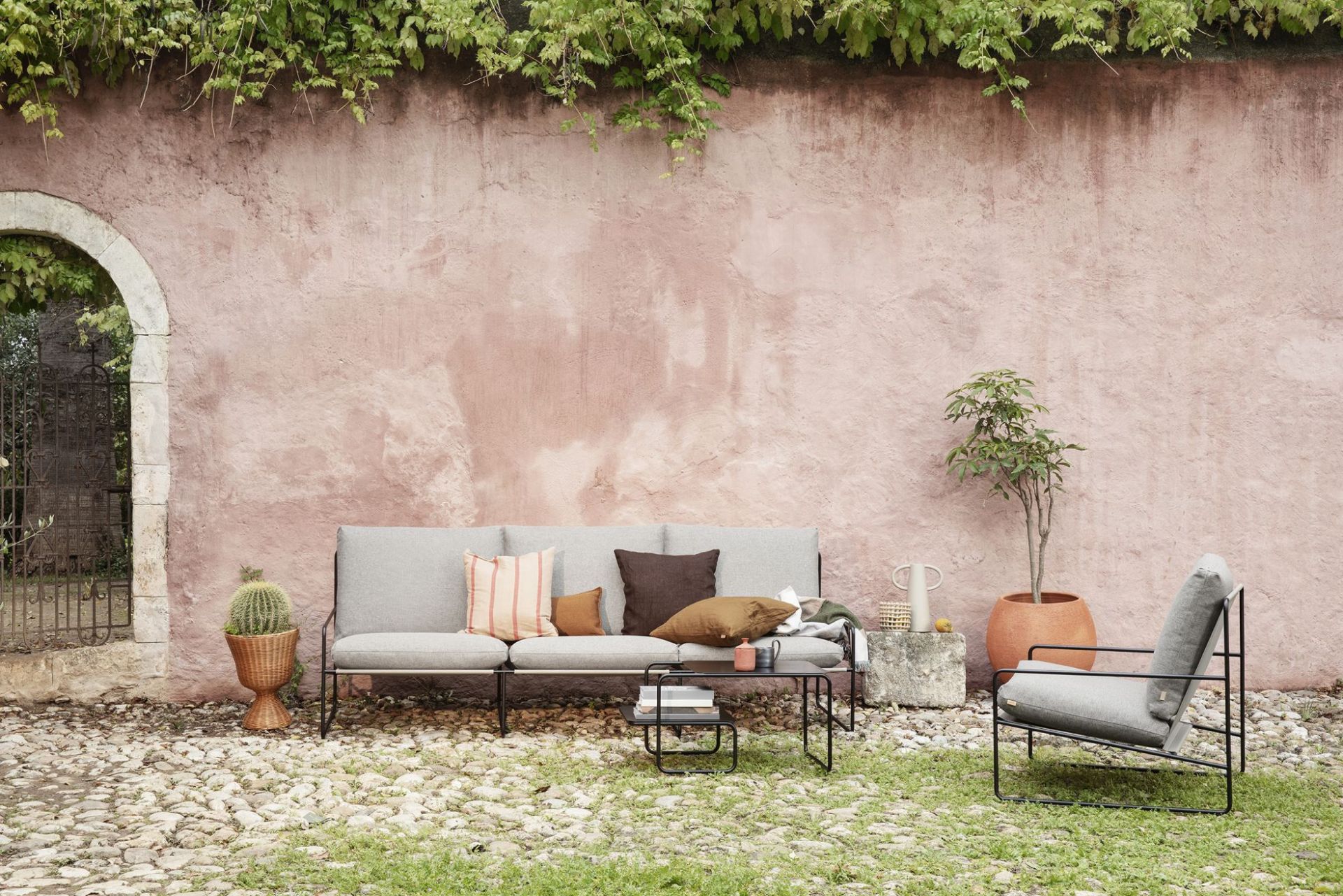 Desert 3-Sitzer Outdoor Sofa von Ferm Living mit schwarzem Gestell und grauer Polsterung im Garten.