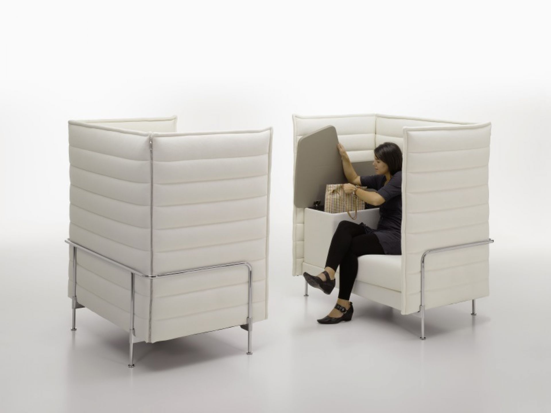 Frau verstaut Tasche im weißen Alcove Highback Sessel von Vitra, Büromöbel für konzentriertes Arbeiten.