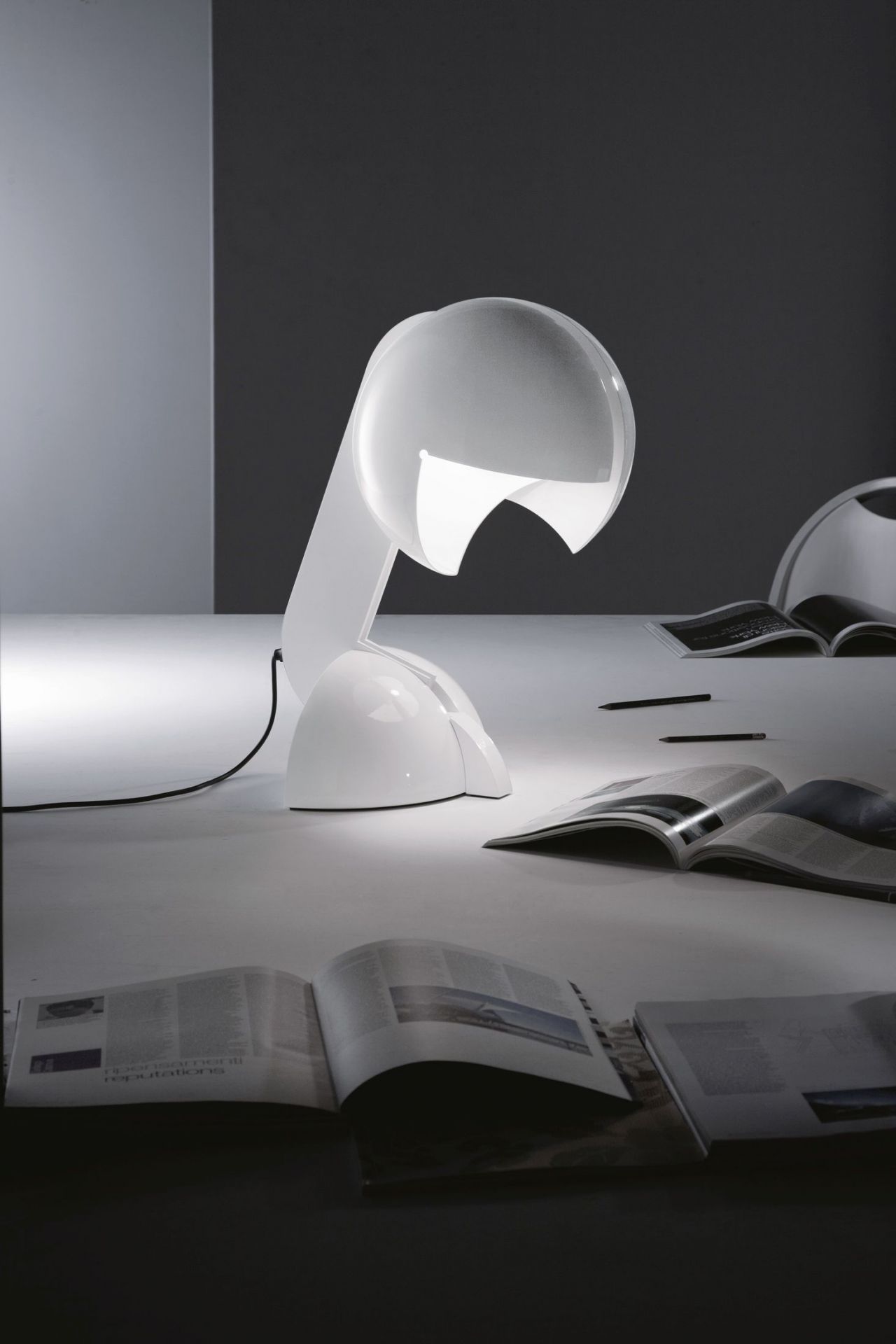 Weiße Ruspa Tischleuchte von Martinelli Luce auf einem Tisch mit Magazinen und Stiften.