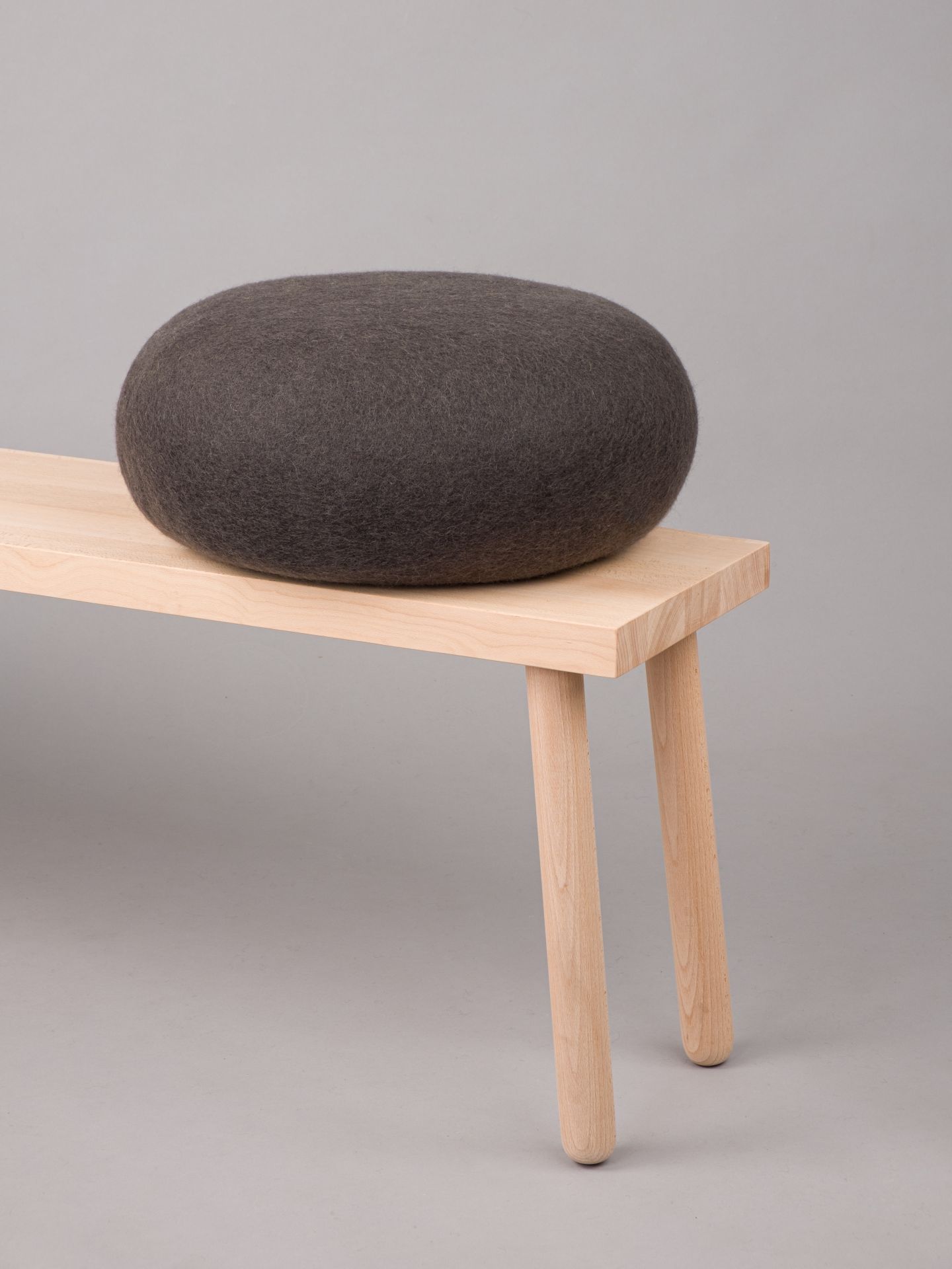 Grauer myfelt Filz Pouf Hocker Kuno auf hellem Holzgestell, modernes Sitzmöbel für Wohnzimmer.