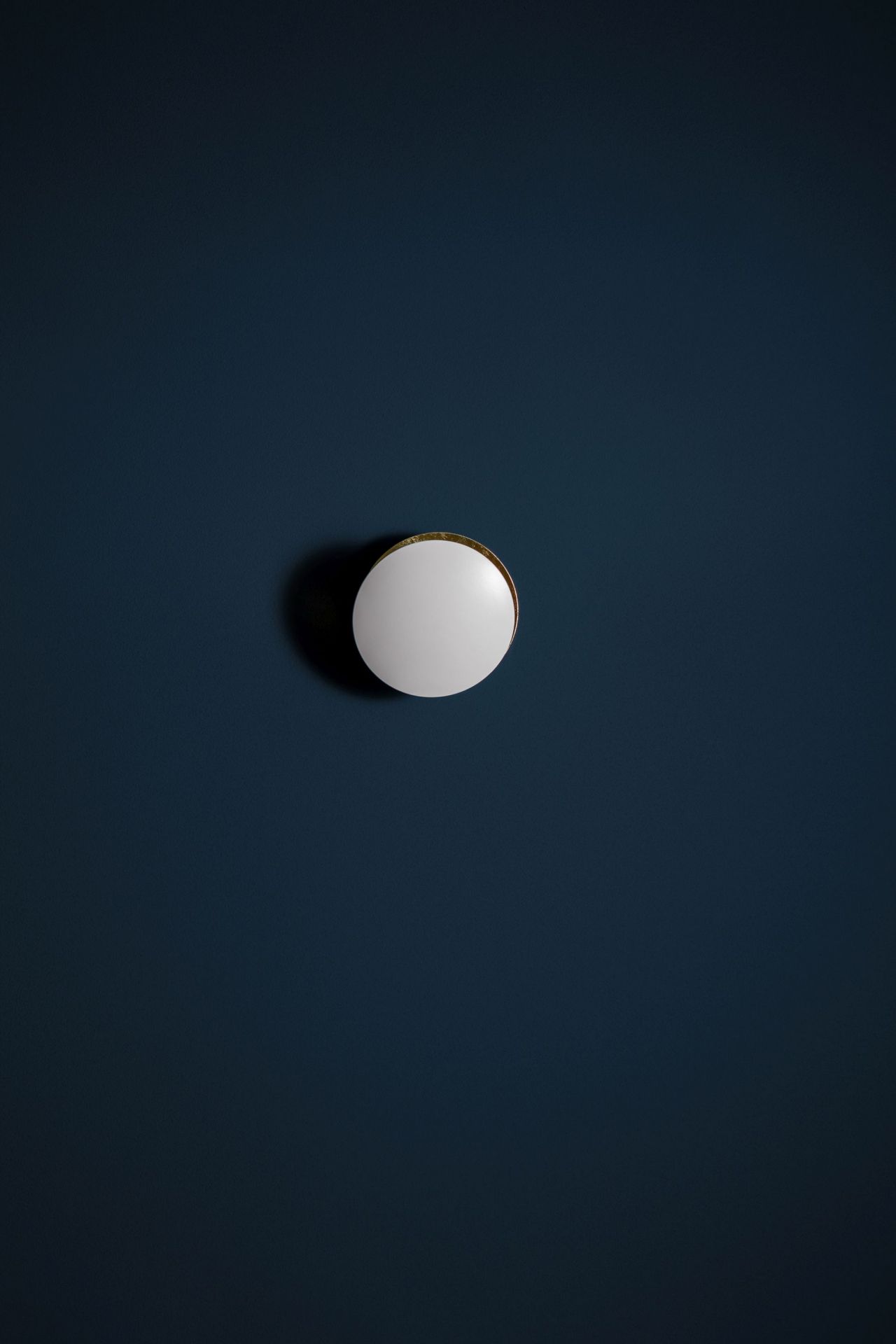 Weiße Lederam Wandleuchte von Catellani & Smith an dunkelblauer Wand. Design Lampe für Wohnzimmer.