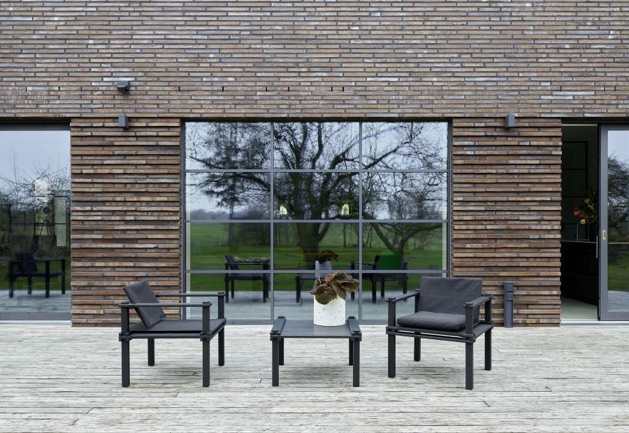 Outdoor-Szene mit Farmer Tisch und passenden Stühlen auf einer Holzterrasse vor einem modernen Haus.