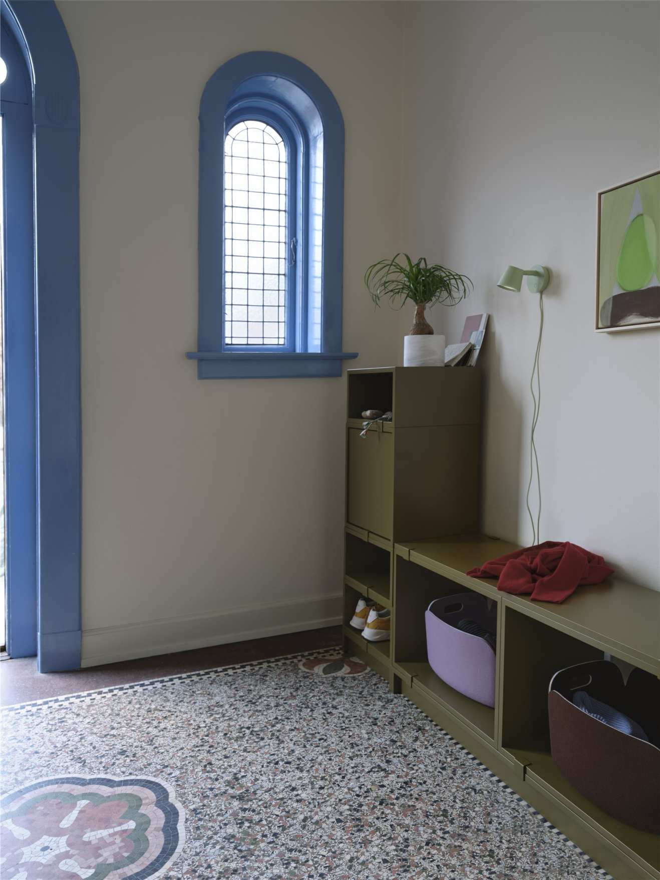 Helle Diele mit Muuto Tip Wall Wandleuchte in Weiß, montiert an der Wand über einem Regal.