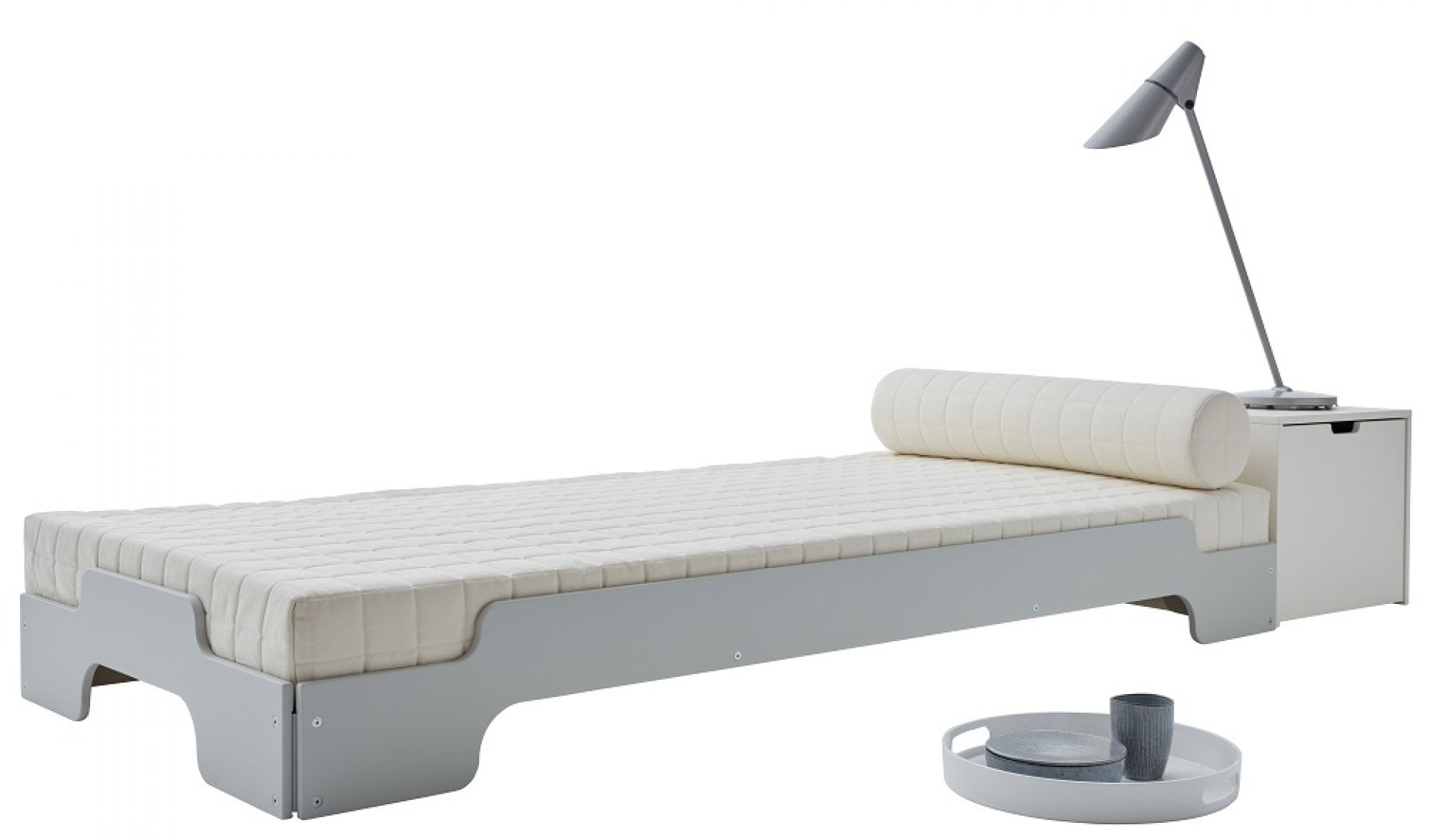Graue Stapelliege Klassik von Müller Möbelwerkstätten mit Matratze, Kissenrolle, Nachttisch und Lampe.