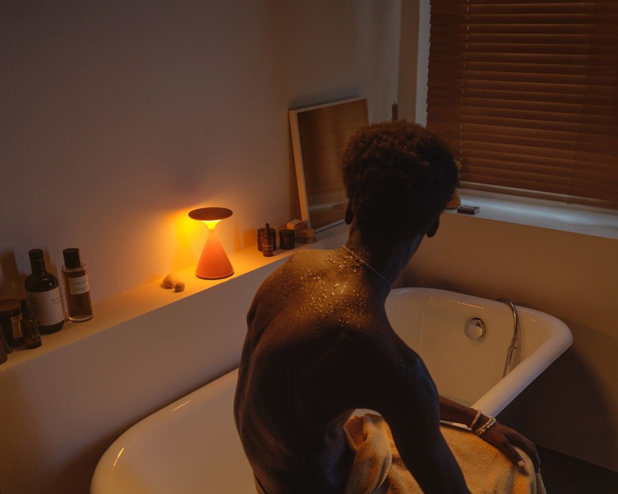 Salt Akkuleuchte in Grau-Sandweiß neben einer Badewanne, stimmungsvolle Tischleuchte für entspannende Momente.