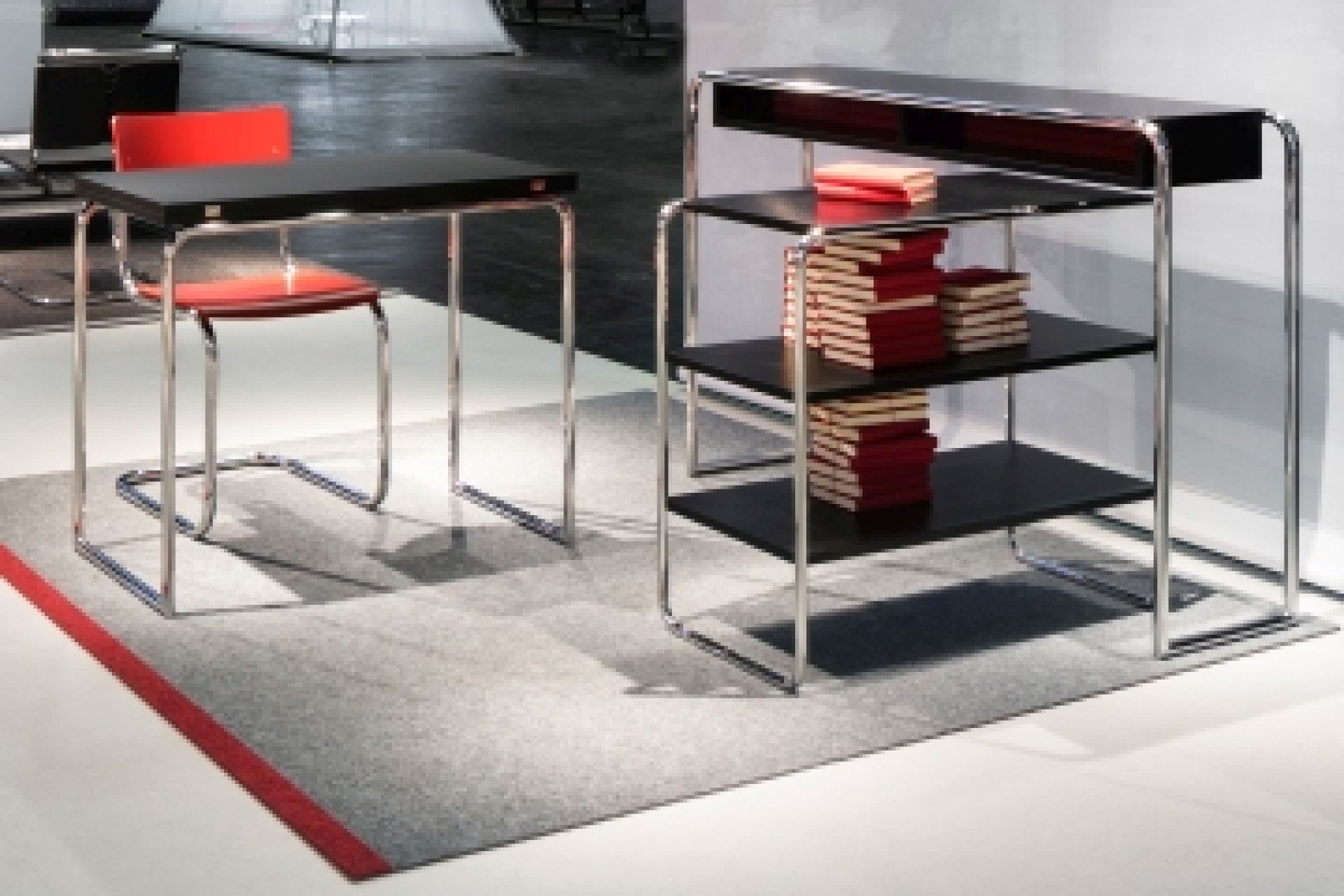 B 22 Stahlrohr Regal von Thonet neben passendem Tisch mit rotem Stuhl. Designklassiker.