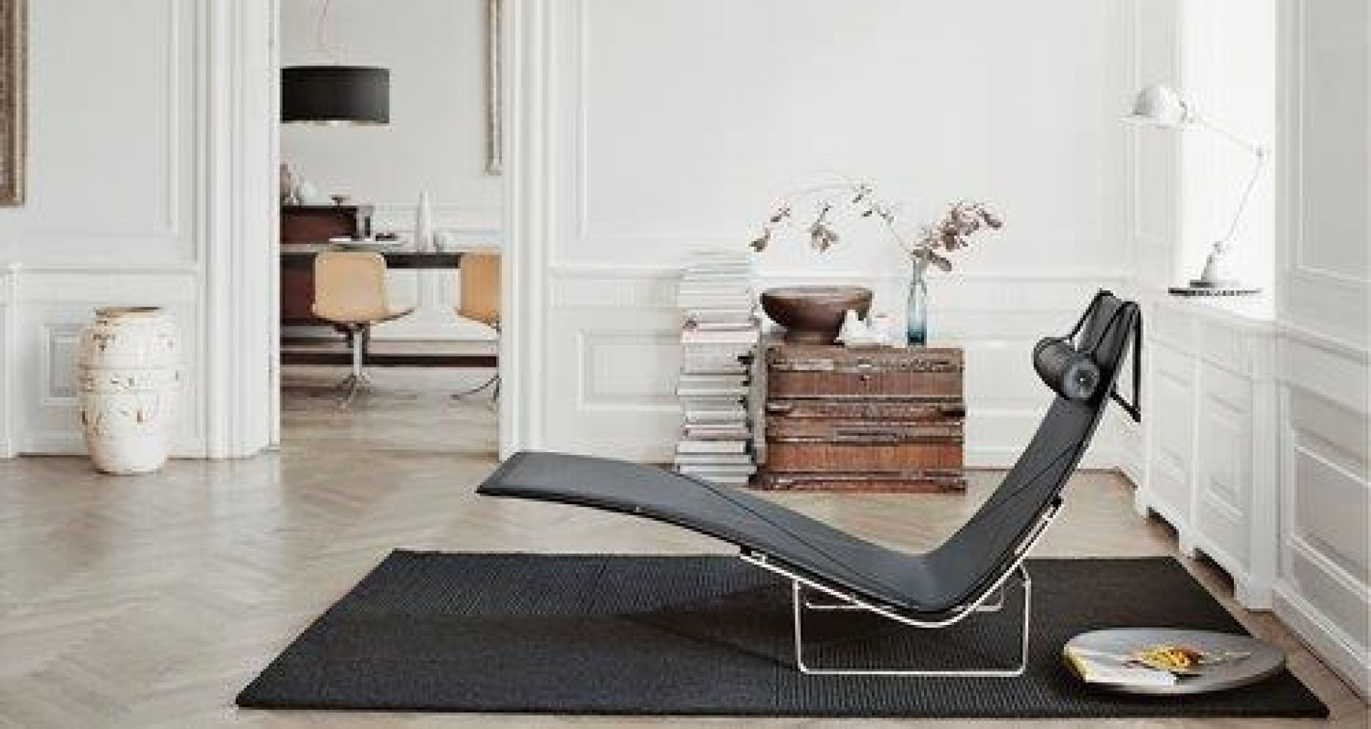 Schwarze PK24 Liege von Fritz Hansen auf dunklem Teppich in einem eleganten Wohnzimmer.