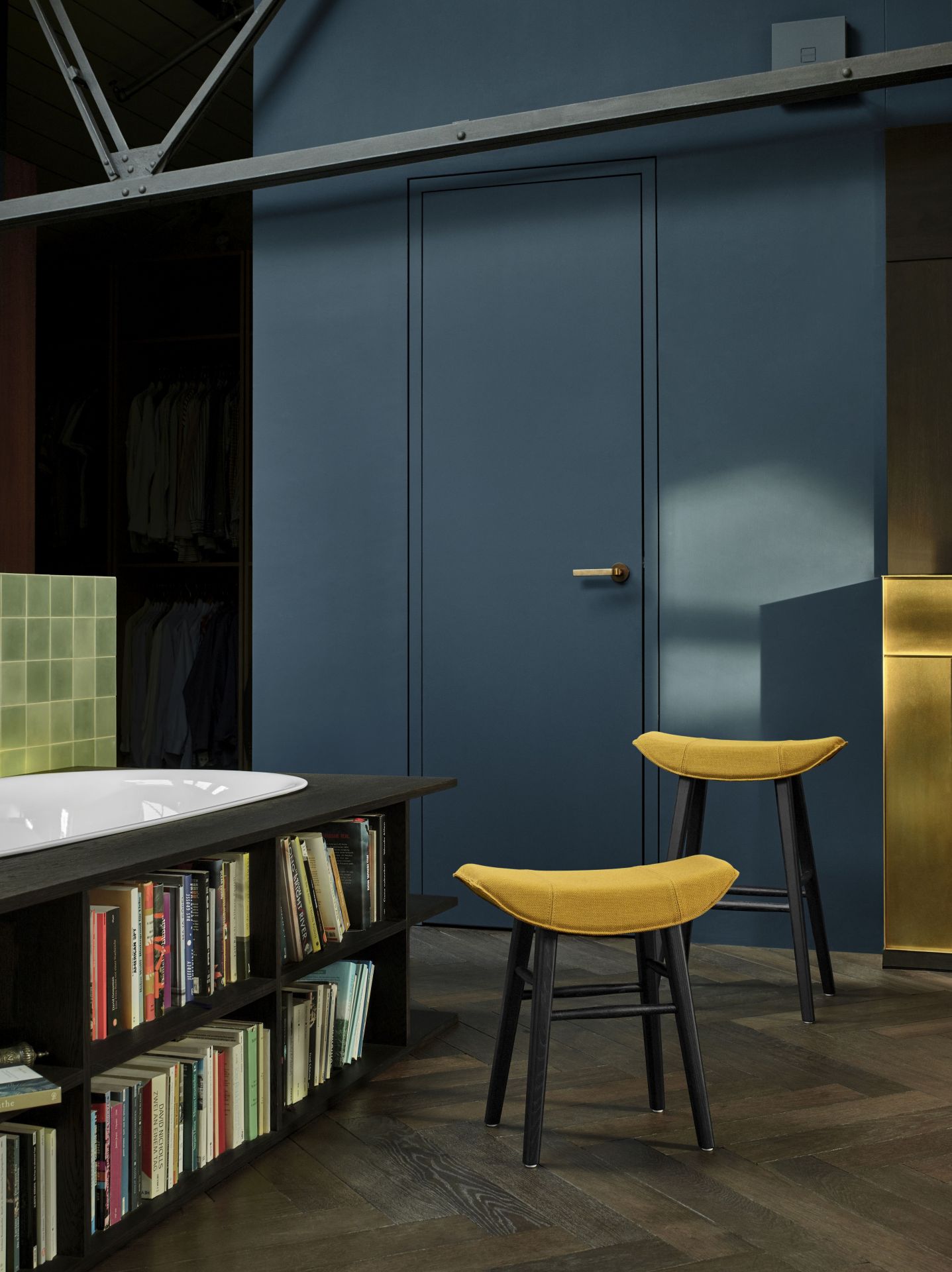 Zwei gelbe Kya Küchenhocker von Freifrau Manufaktur vor blauer Wand und Bücherregal.