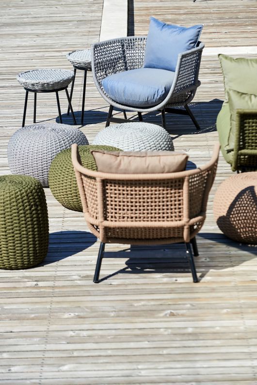 Outdoor-Szene mit Suka Lounge Sessel von Jan Kurtz, Poufs und Beistelltischen auf einer Holzterrasse.