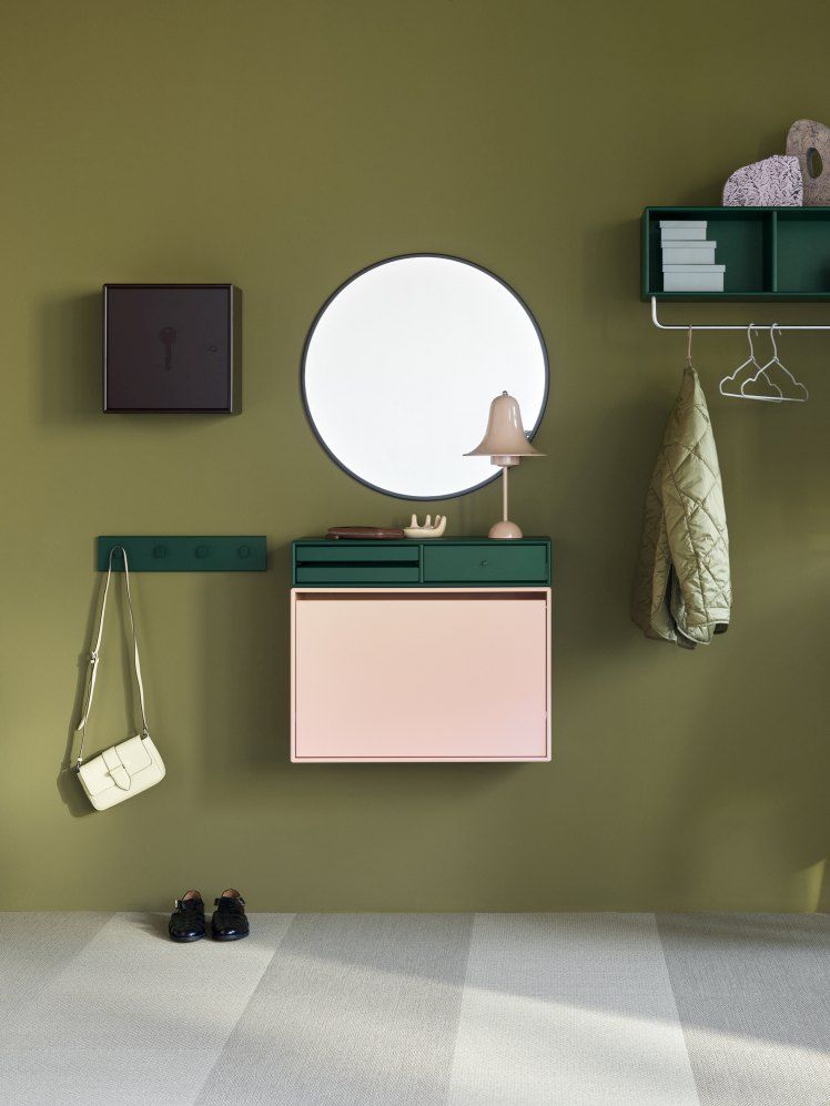 Ein runder Spiegel mit schwarzem Rahmen, Modell Montana Rosehip, an einer grünen Wand.