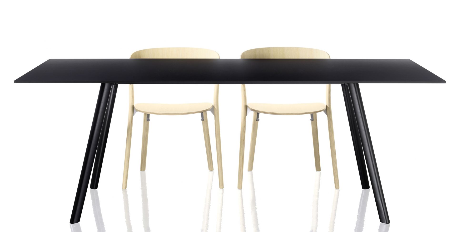 Zwei helle Holzstühle vom Typ Pila Stuhl stehen an einem schwarzen Esstisch.