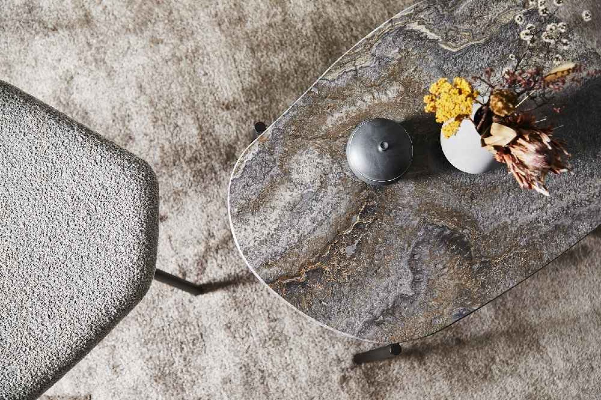 Grau melierter La Terra Couchtisch von Woud mit Blumen und Dose auf einem Teppich.