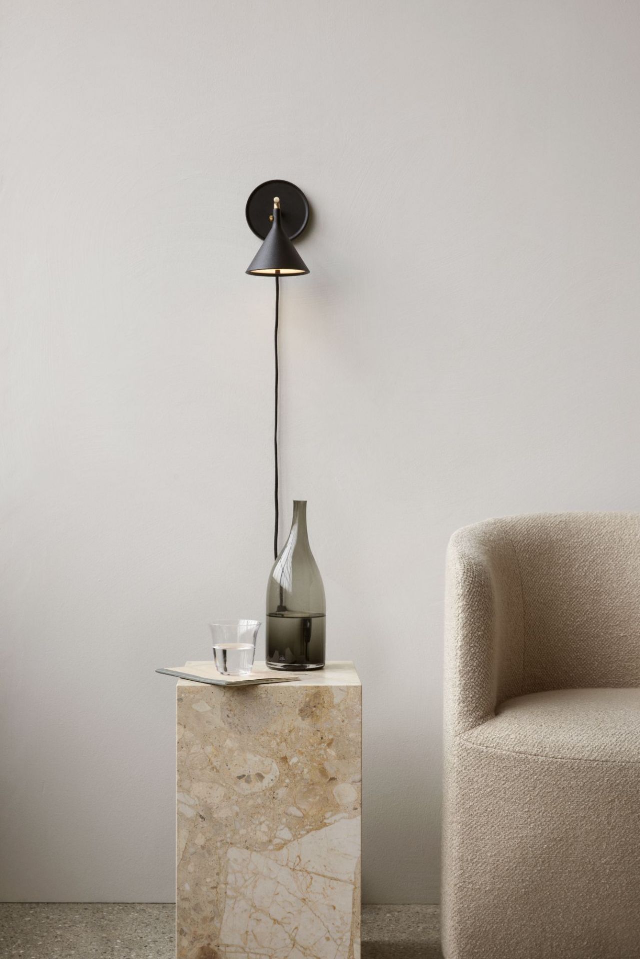 Audo Tearoom Sofa in Beige neben Marmortisch mit Wasserflasche und schwarzer Wandlampe.