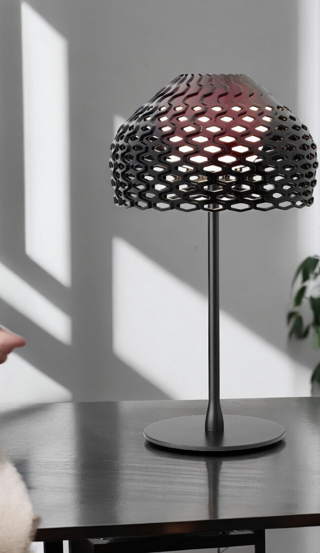 Schwarze Tatou T1 Tischleuchte von Flos mit filigranem Lampenschirm auf einem dunklen Tisch.