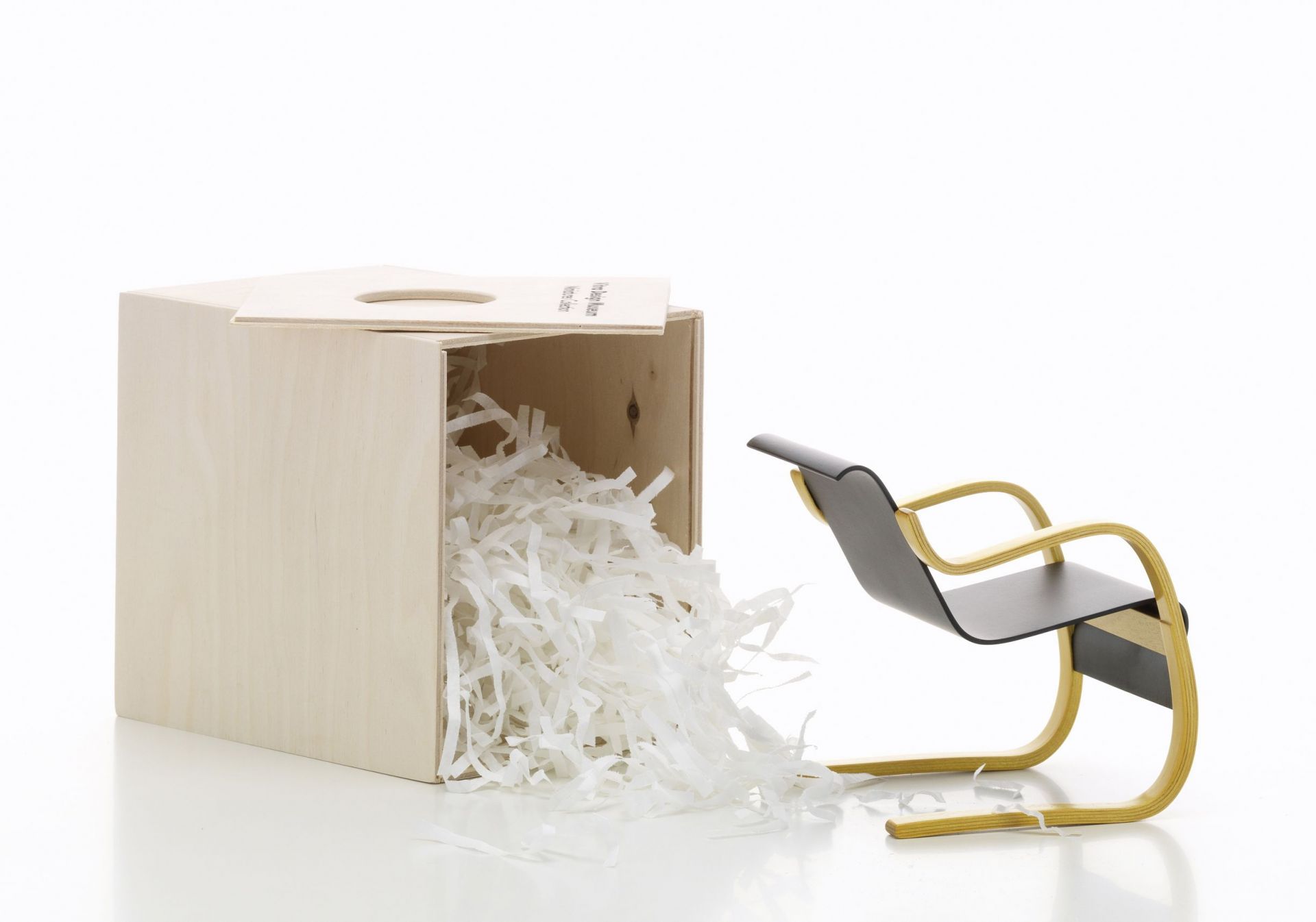 Miniatur Sessel Nr. 42 von Vitra neben einer Holzkiste mit Papierstreifen. Designmöbel.