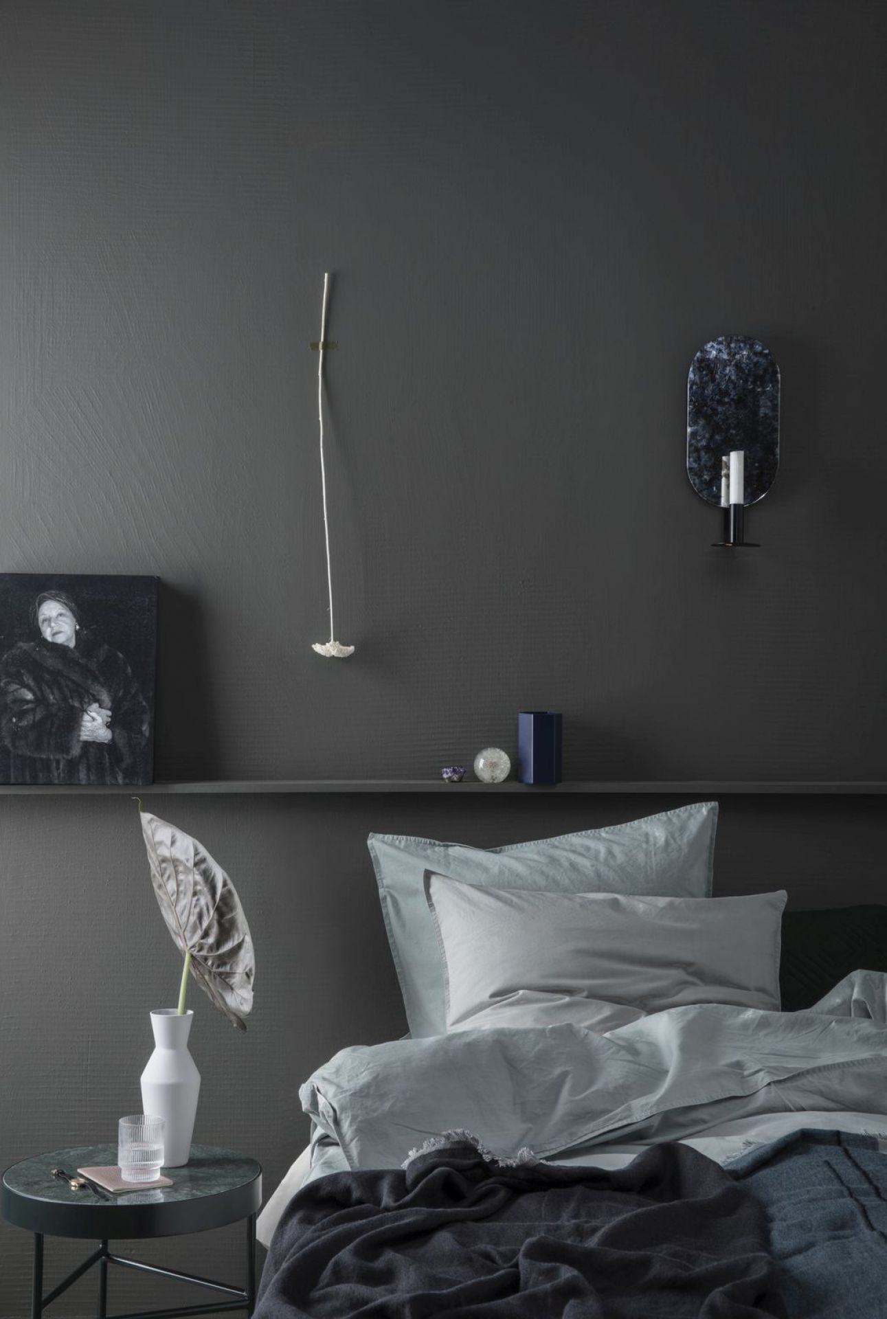 Ferm Living Beistelltisch aus Marmor neben einem Bett in einem dunkelgrauen Schlafzimmer.