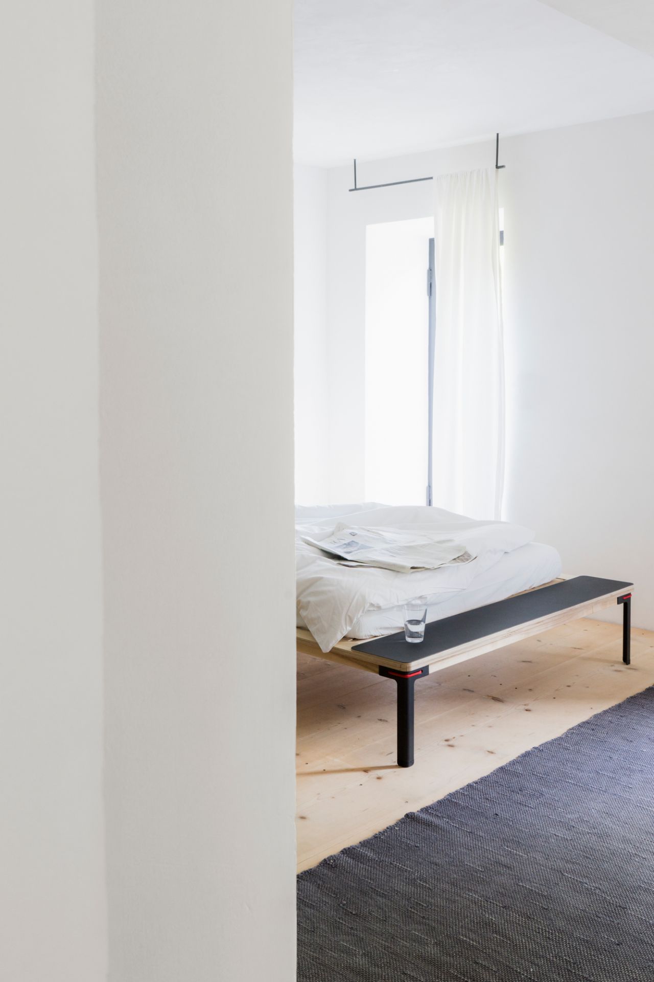 Rotes Seiltänzer Bett 160x200 von Nils Holger Moormann im minimalistischen Schlafzimmer mit Teppich.