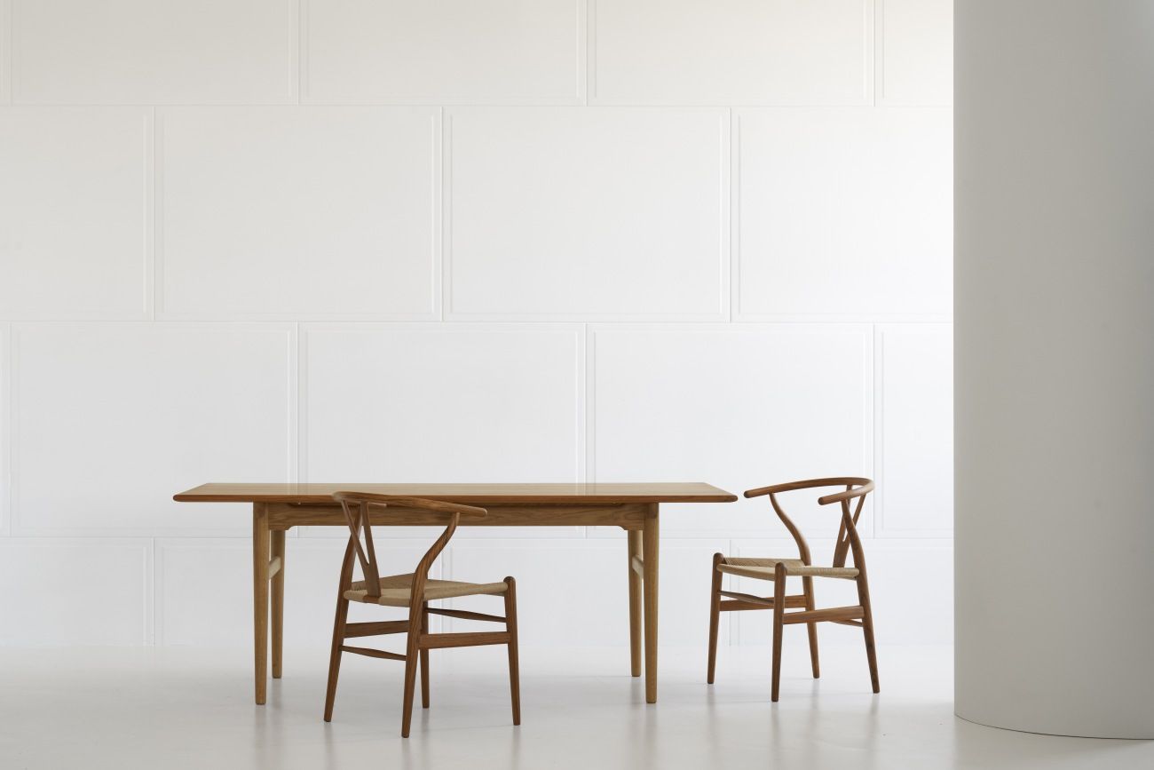 CH327 Esstisch Teak von Carl Hansen & Søn mit zwei Holzstühlen vor weißer Wand.