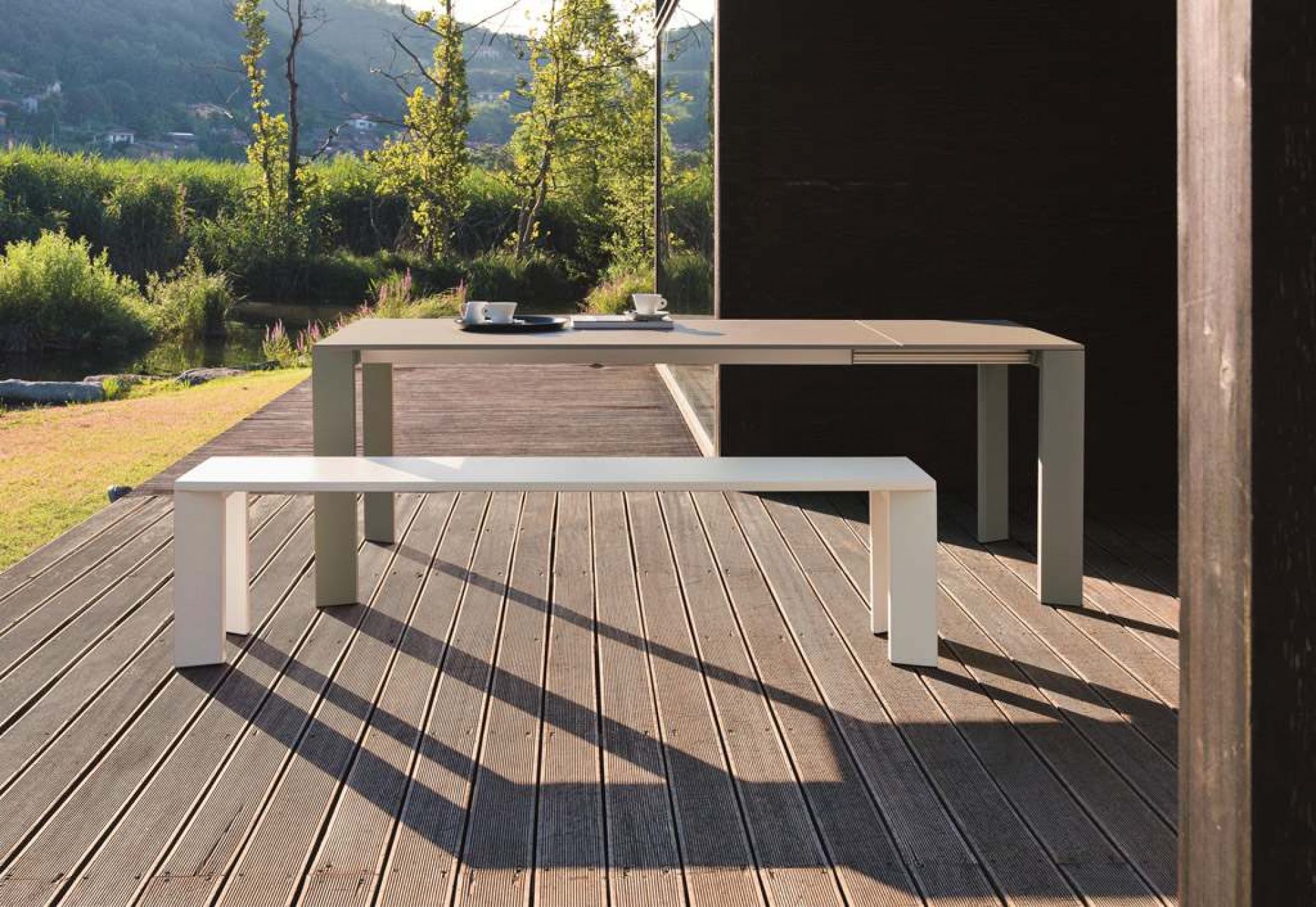 Weiße Grande Arche Outdoor Bank aus Metall vor passendem Esstisch auf Holzterrasse.