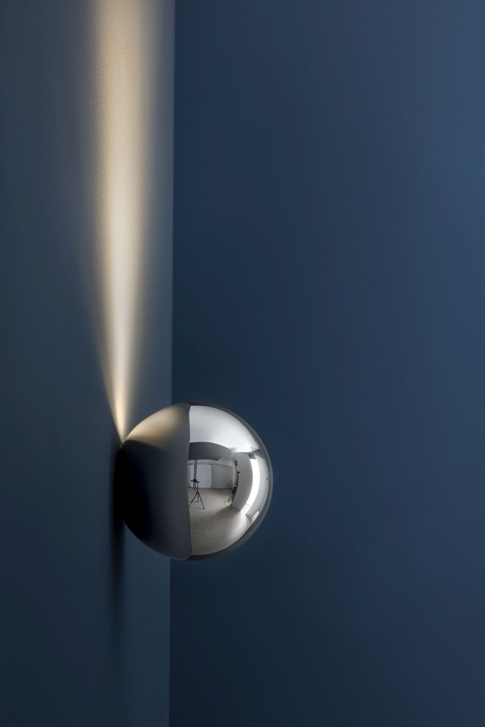 Sfera Wandleuchte von Catellani & Smith: Runde, silberne Wandlampe mit indirektem Licht an blauer Wand.