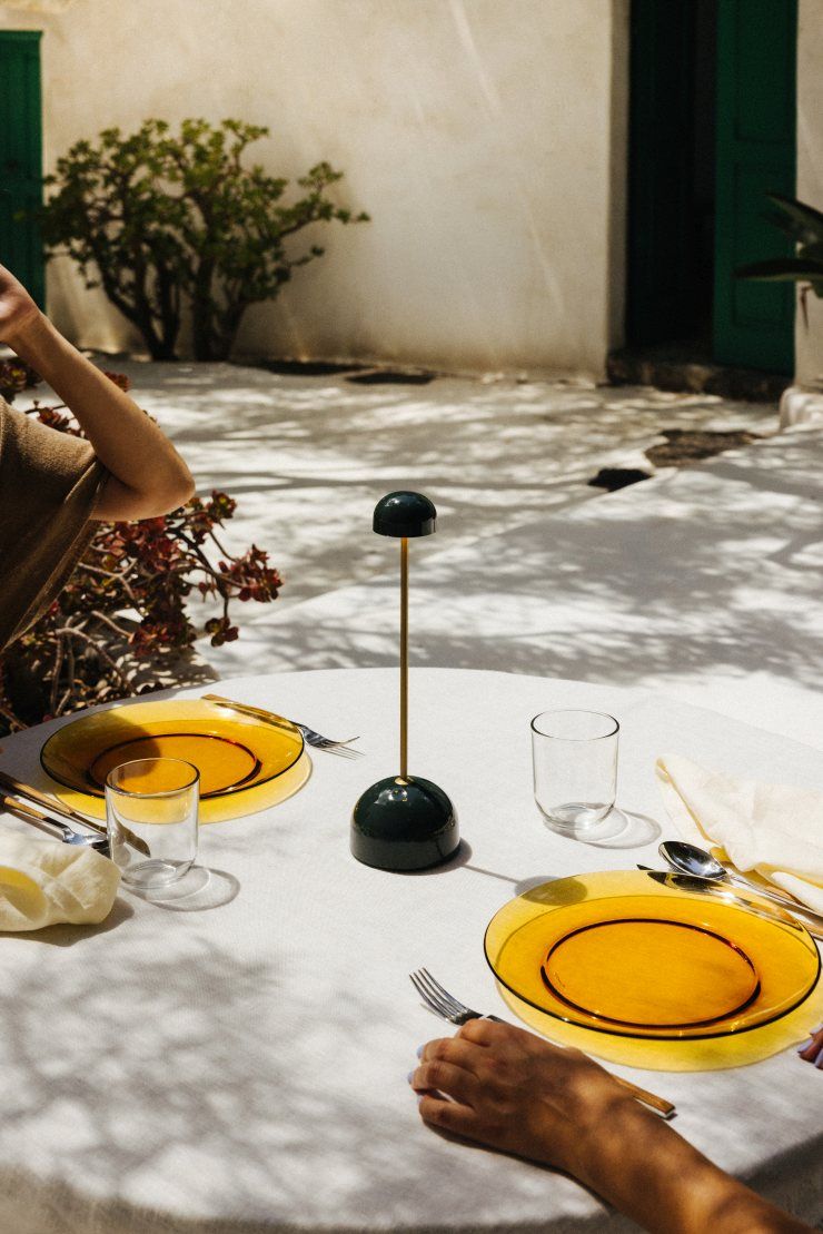 Sips Akkuleuchte in Grün/Gold von Marset auf gedecktem Tisch im Freien.