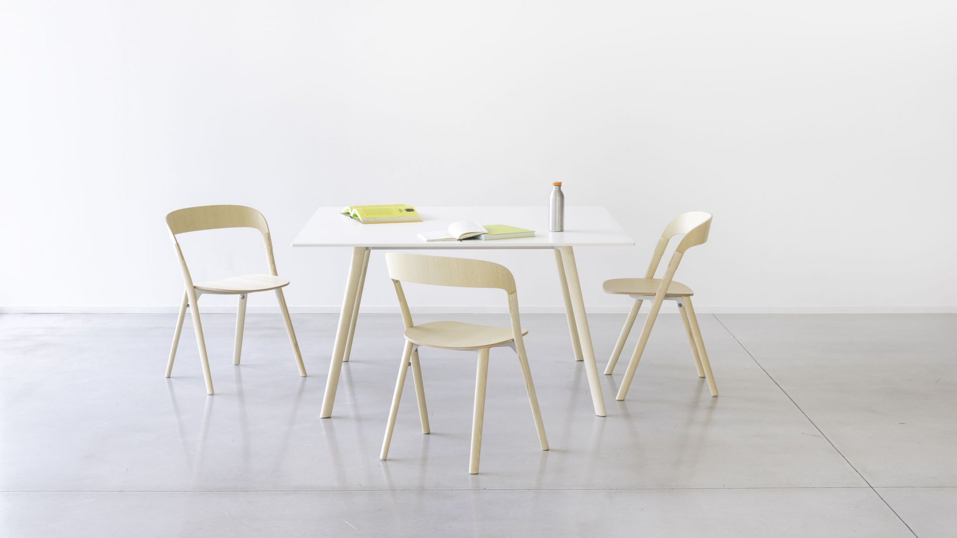 Drei helle Holzstühle vom Typ Pila Stuhl um einen weißen Tisch im minimalistischen Design.