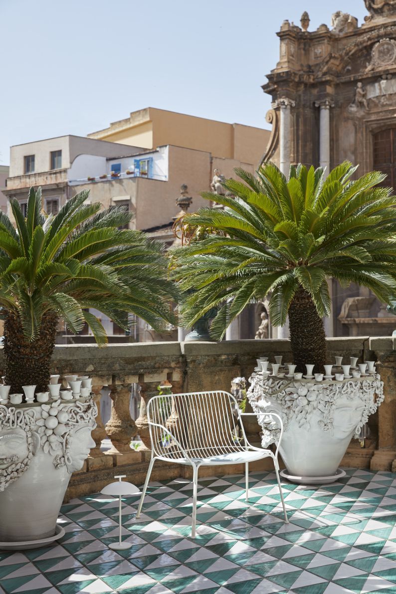 Weißer Hiray Outdoor Sessel von Kartell auf einem Balkon mit Pflanzen und Fliesen.