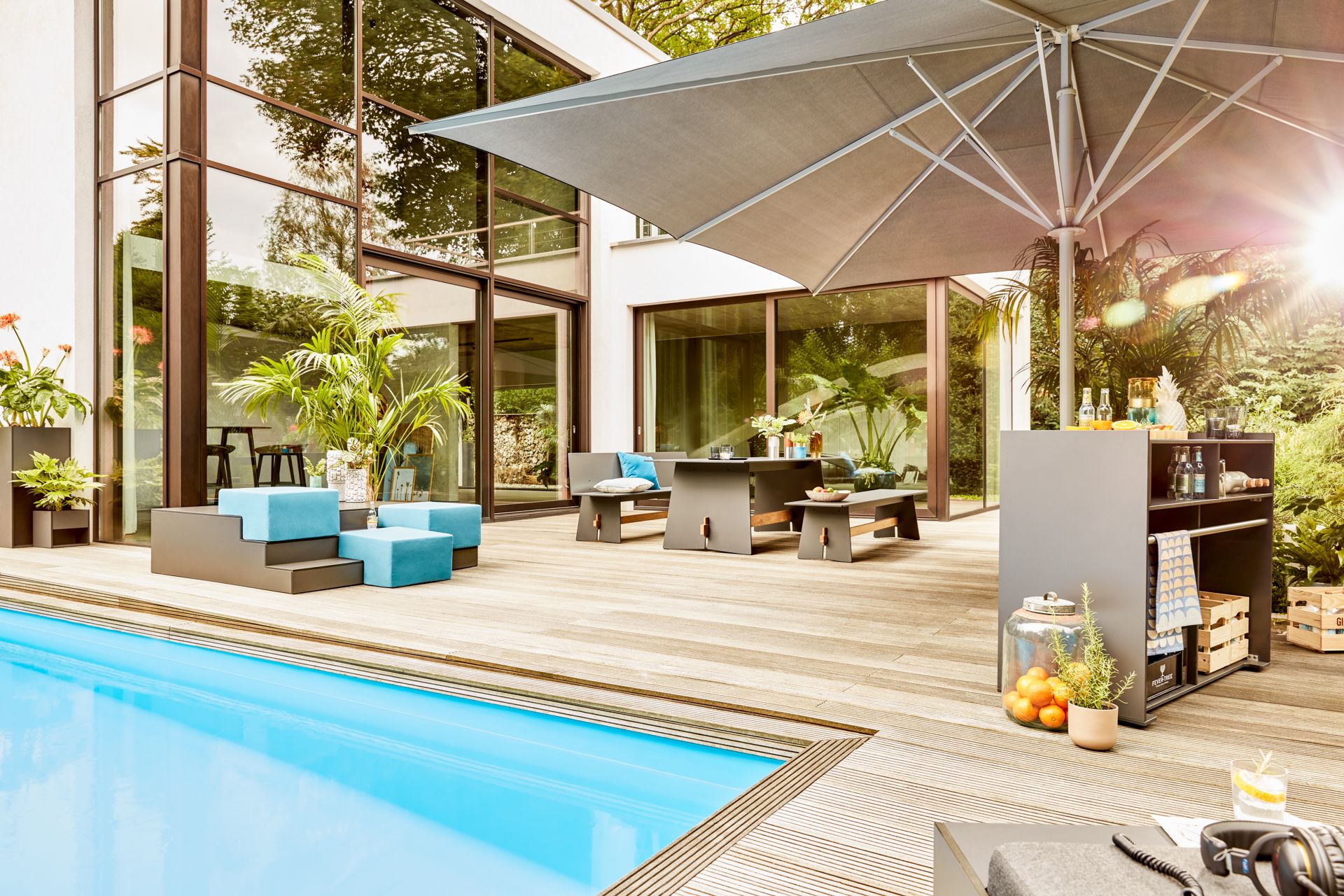 Conmoto Tension Outdoor Esstisch mit Bänken in Anthrazit auf einer Holzterrasse neben einem Pool.