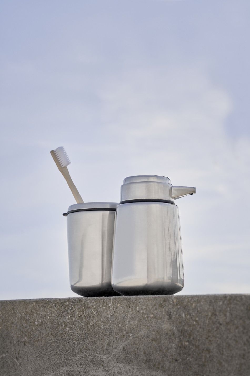 Vipp Zahnbürstenhalter aus Edelstahl mit Zahnbürste und Seifenspender vor hellem Himmel. Badaccessoires für moderne Badezimmer.