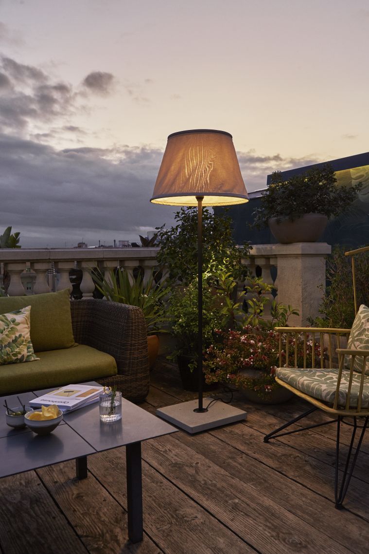 Beige TXL Stehleuchte von Marset beleuchtet abends eine Terrasse mit Loungemöbeln und Pflanzen.