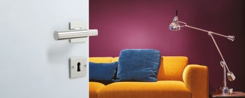 Walter Gropius Türdrücker Tecnolumen Nickel poliert an weißer Tür, im Hintergrund modernes Wohnzimmer.